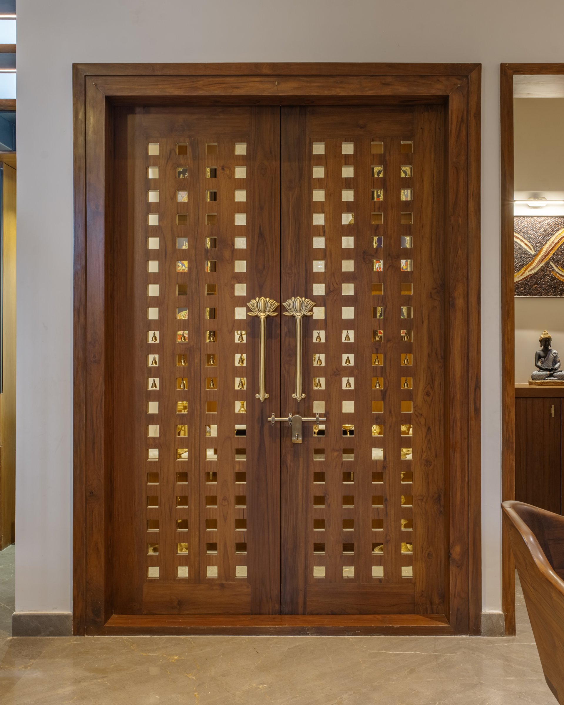The pooja doors closed, a pair of teak leaves perforated with a grid of small square openings and lotus-form handles