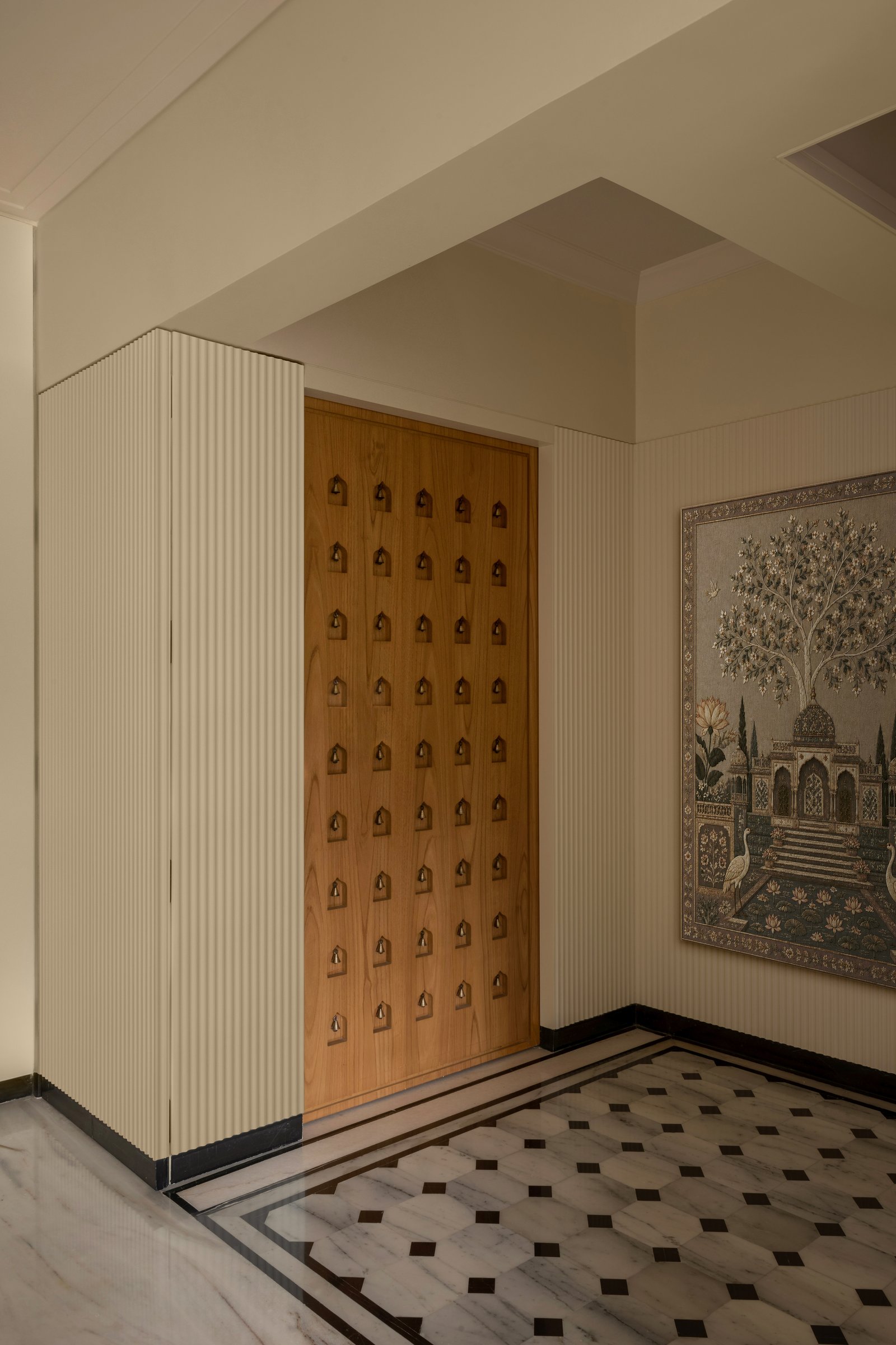 The entry: a patterned wooden door flanked by fluted panelling and a botanical wall panel, grounded on chequered marble