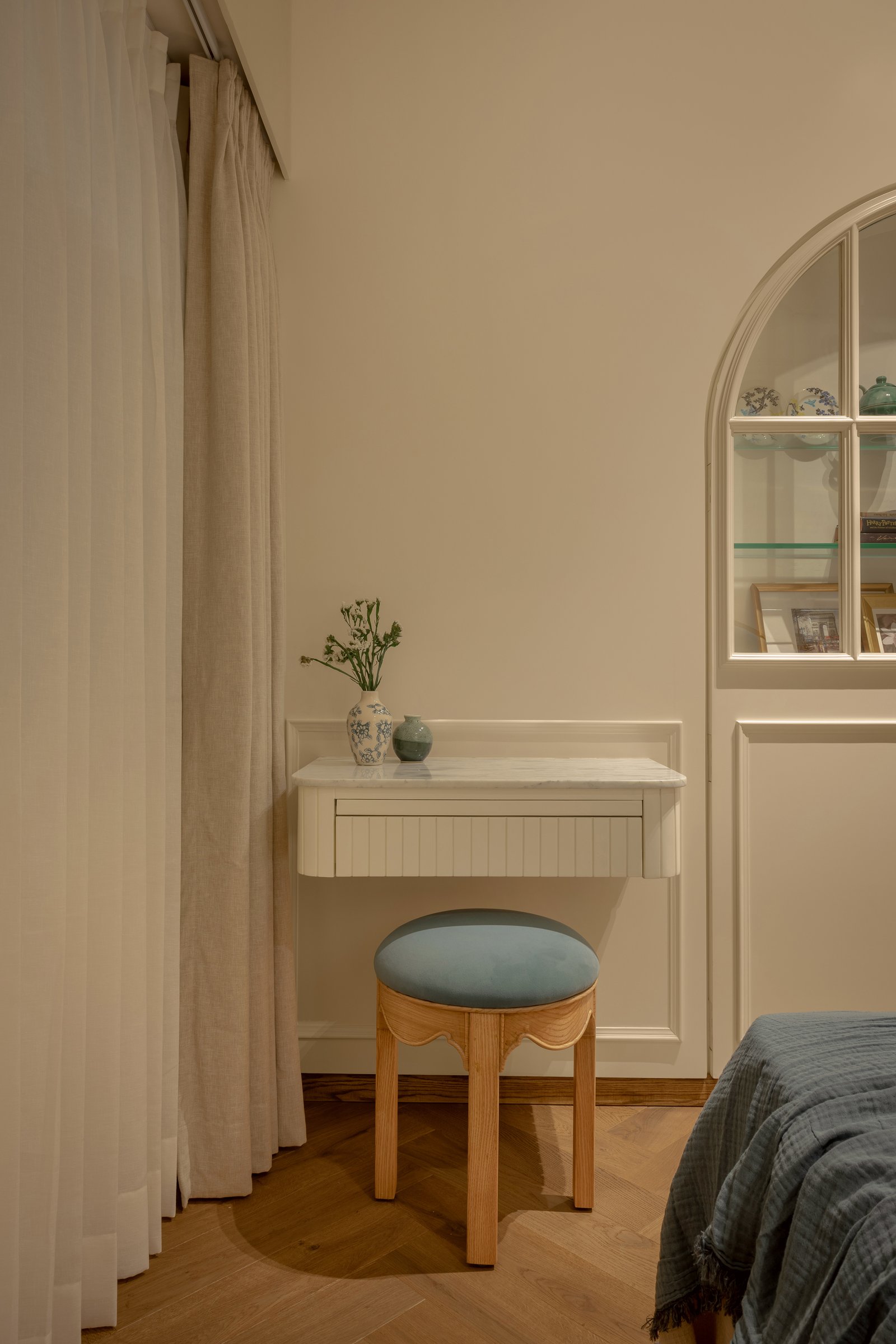 A wall-mounted dressing surface with a fluted skirt and a rounded wooden stool