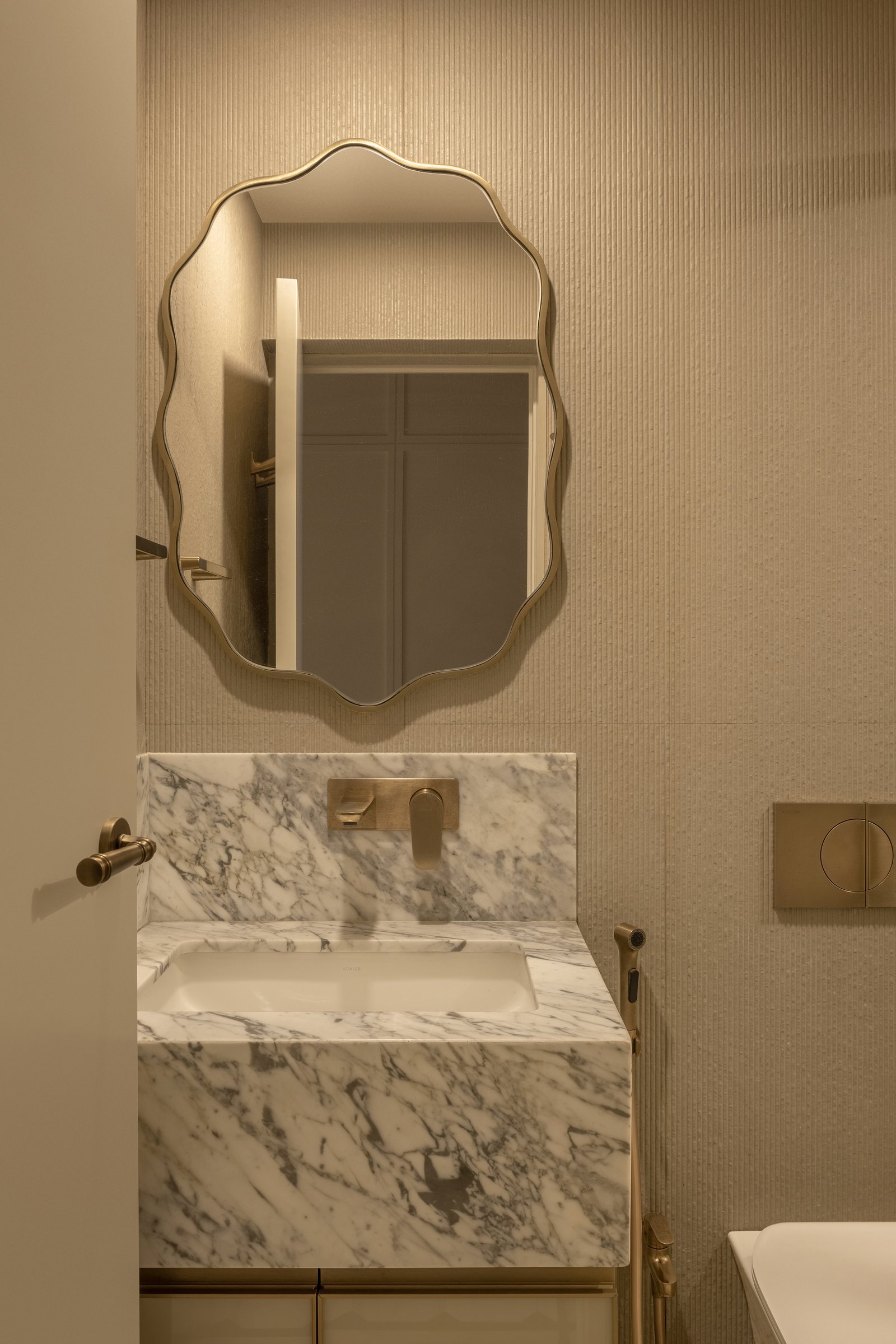 The bathroom vanity, with a wavy-edged mirror above marble and brass