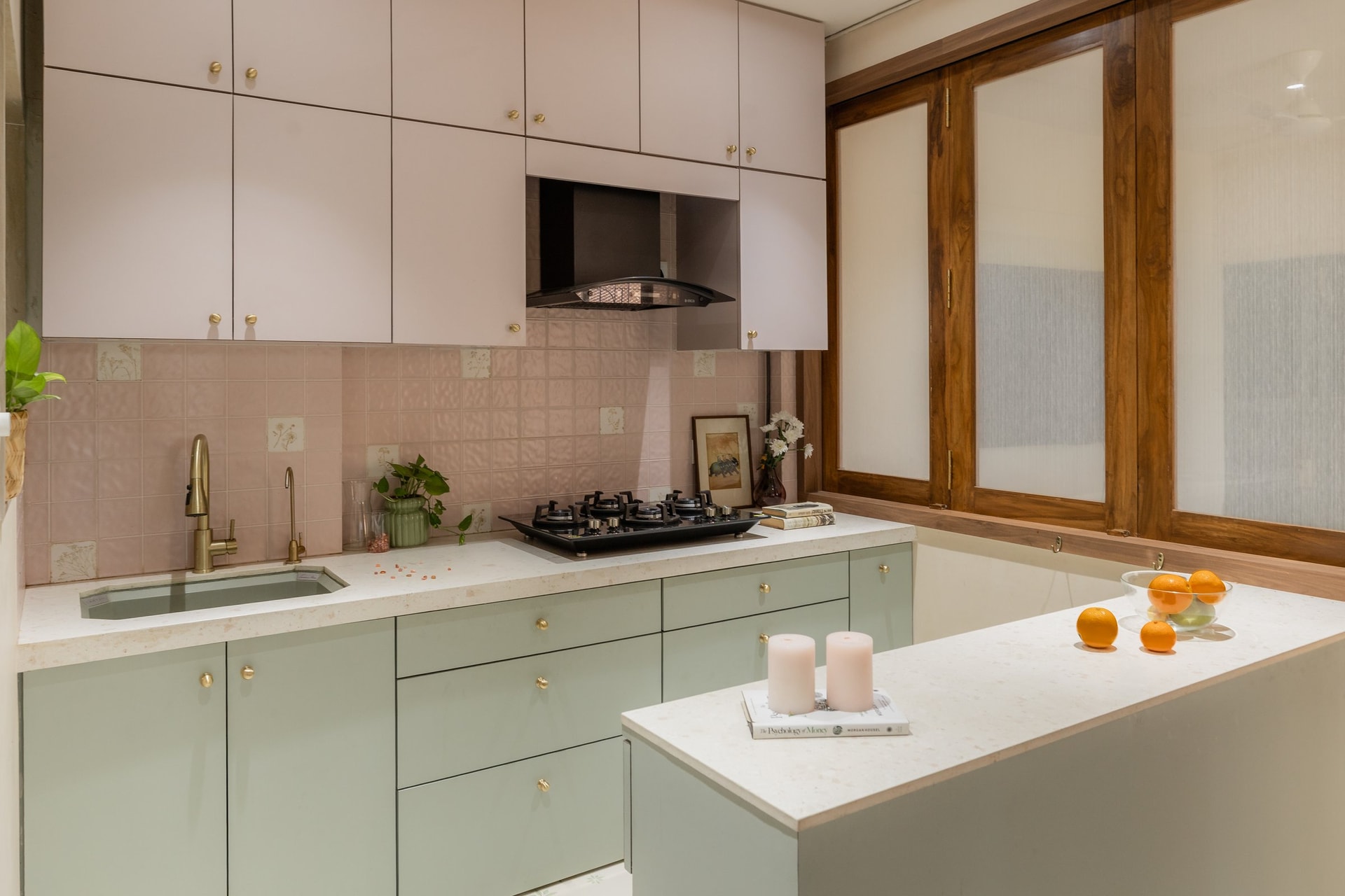 The kitchen, where sage-green base cabinetry meets pale-pink uppers under a wooden-framed partition