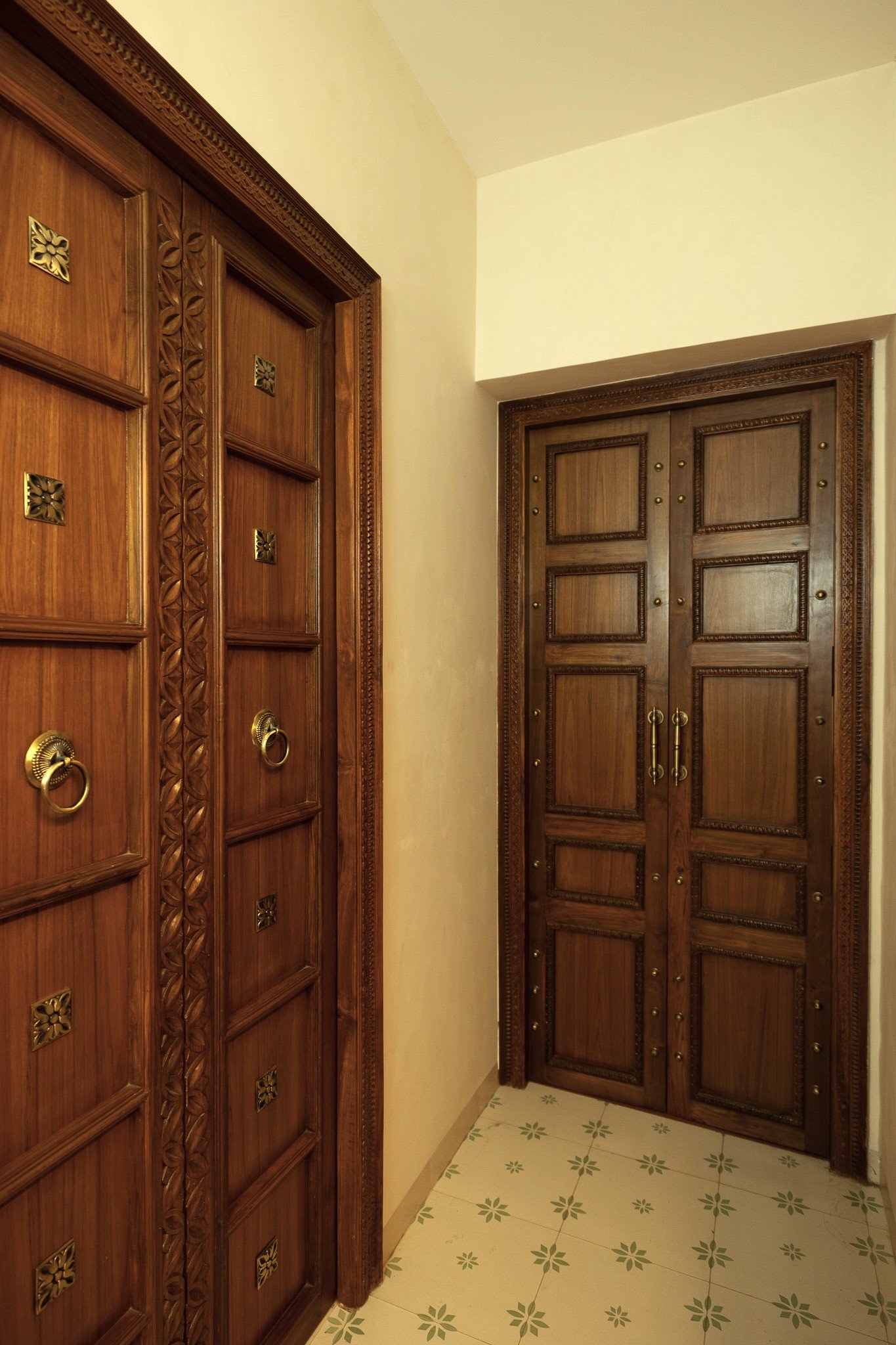 The entry doors, panelled and studded with brass, open onto a green-and-cream cement-tile passage