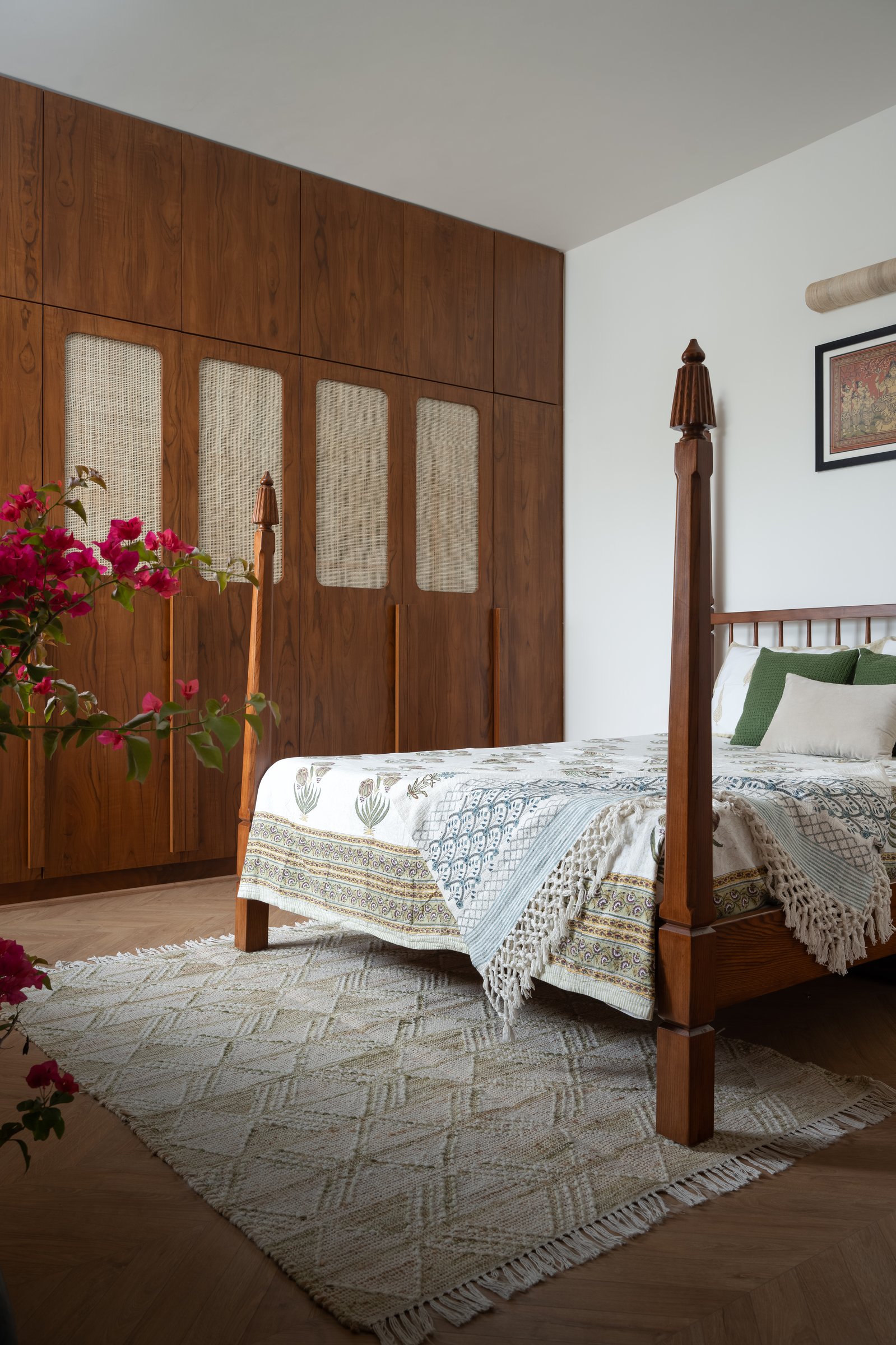 In the master bedroom, a four-poster bed sits against a wall of hardwood wardrobes with woven cane insets
