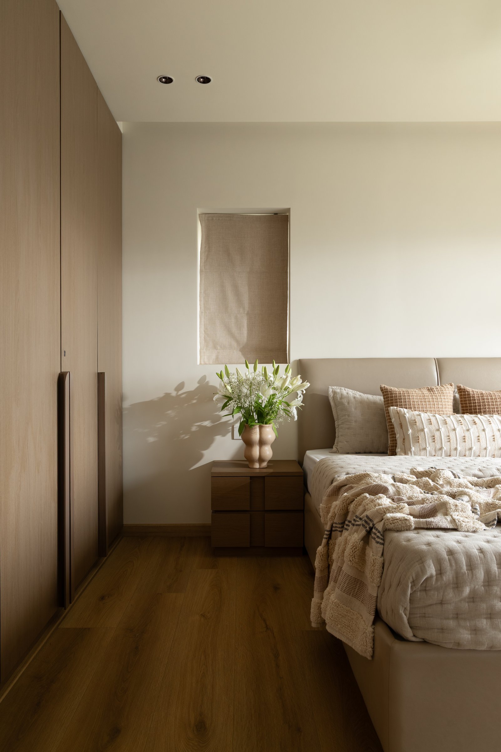 The master bedroom, where a wall of warm-timber wardrobes runs beside an upholstered bed