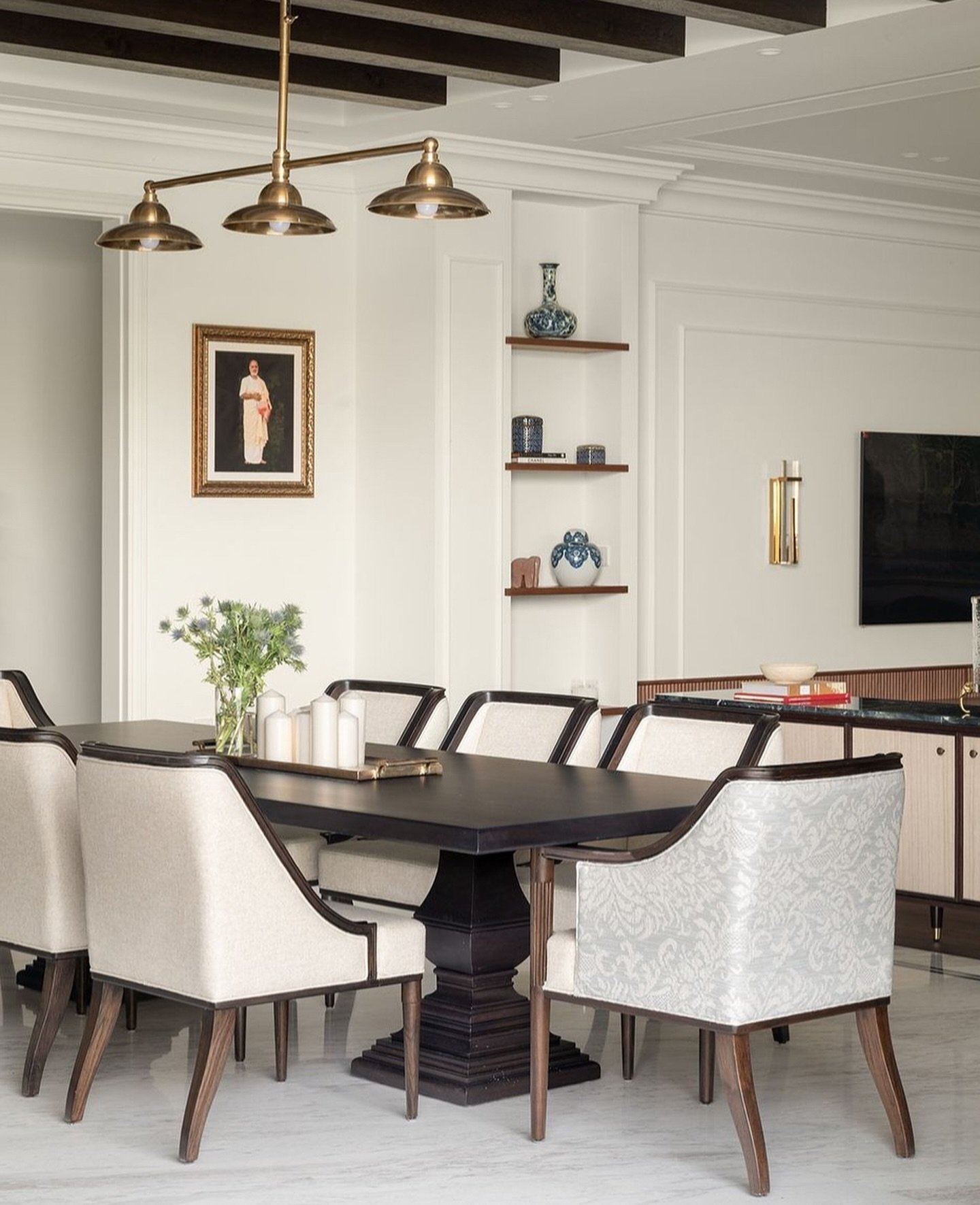 A formal dining room anchored by a brass pendant and a niche of blue-and-white ceramics.