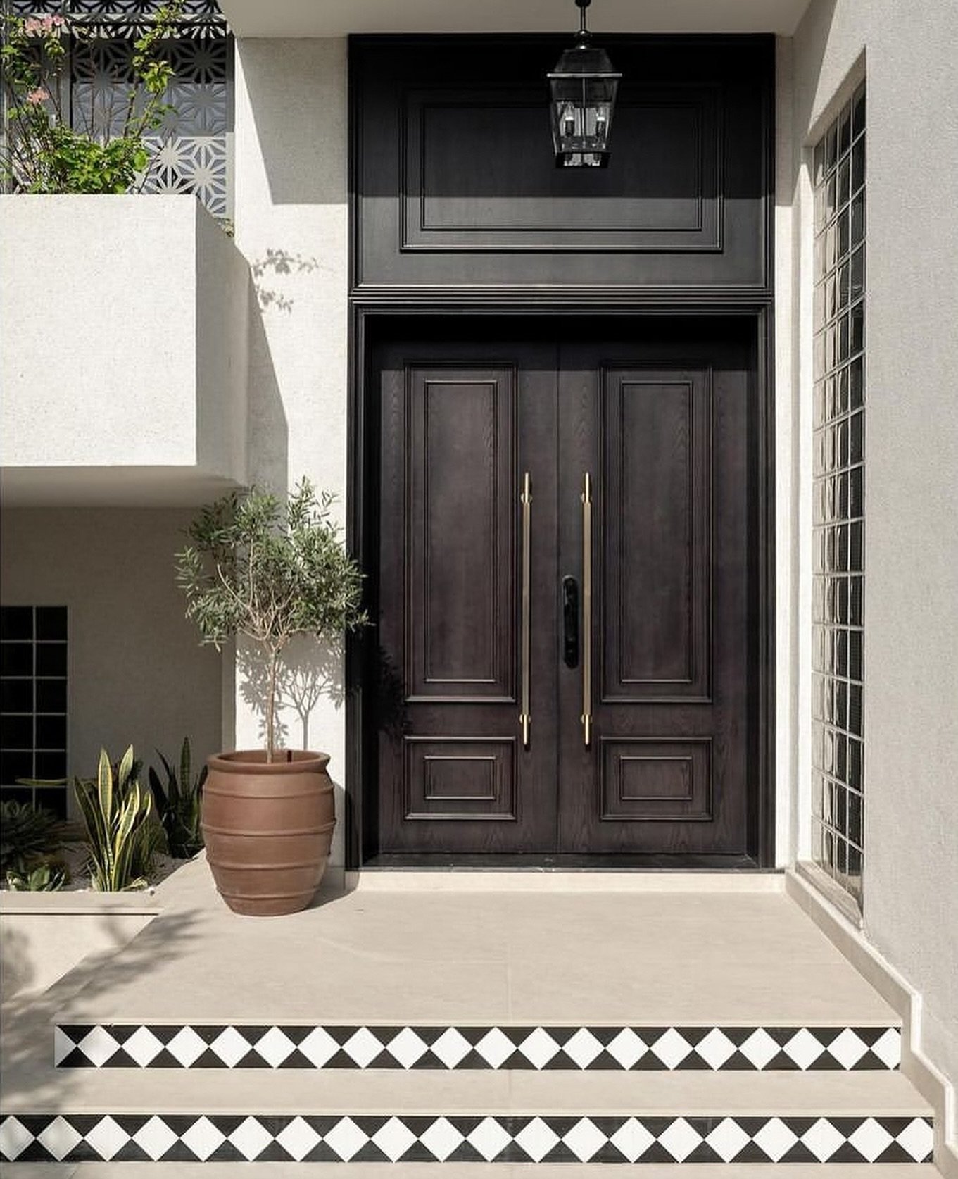 The entrance: dark wood paneling, brass handles, and an olive tree on a stone landing.