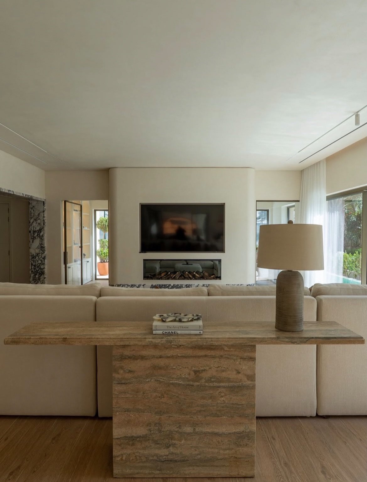 A curved plaster wall organises the living room around a recessed fireplace and bookmatched travertine console.