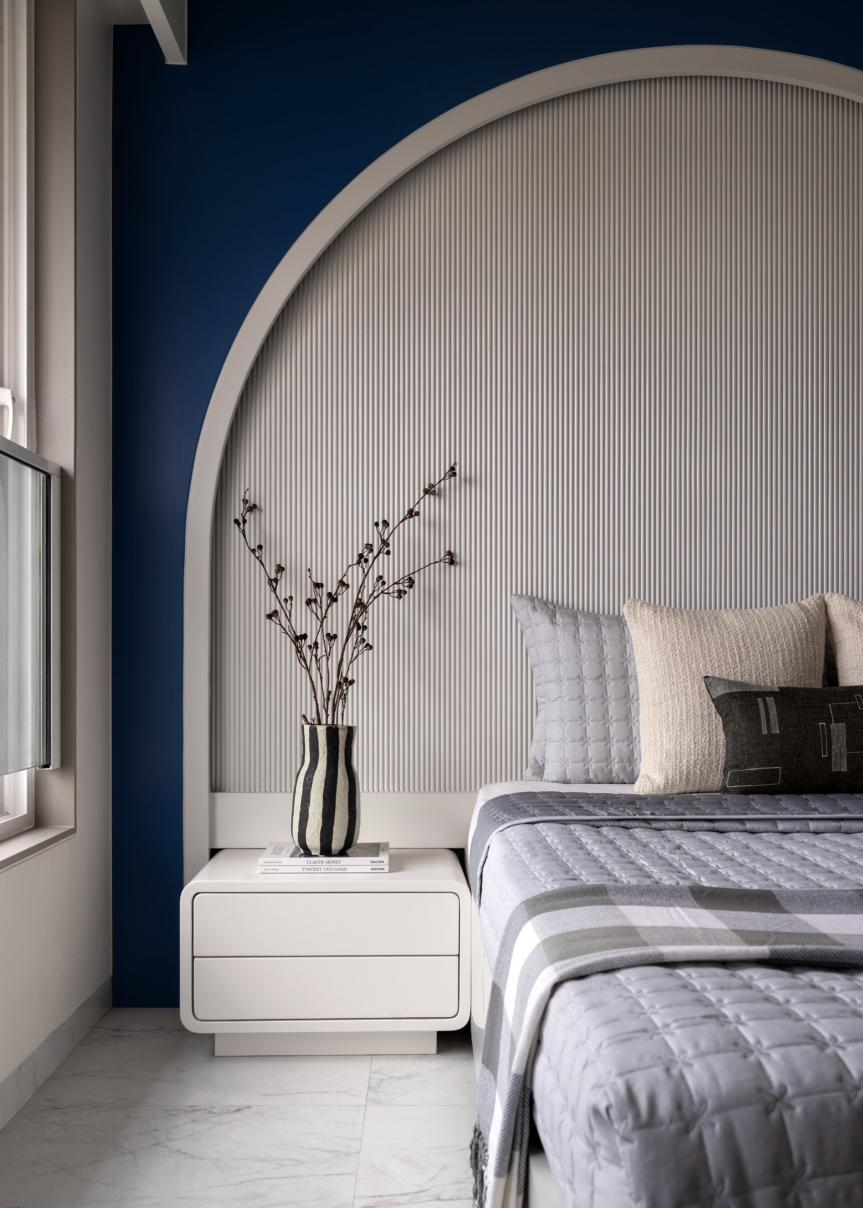 A closer view of the arch, with a rounded ivory nightstand holding a striped vase and stacked art volumes
