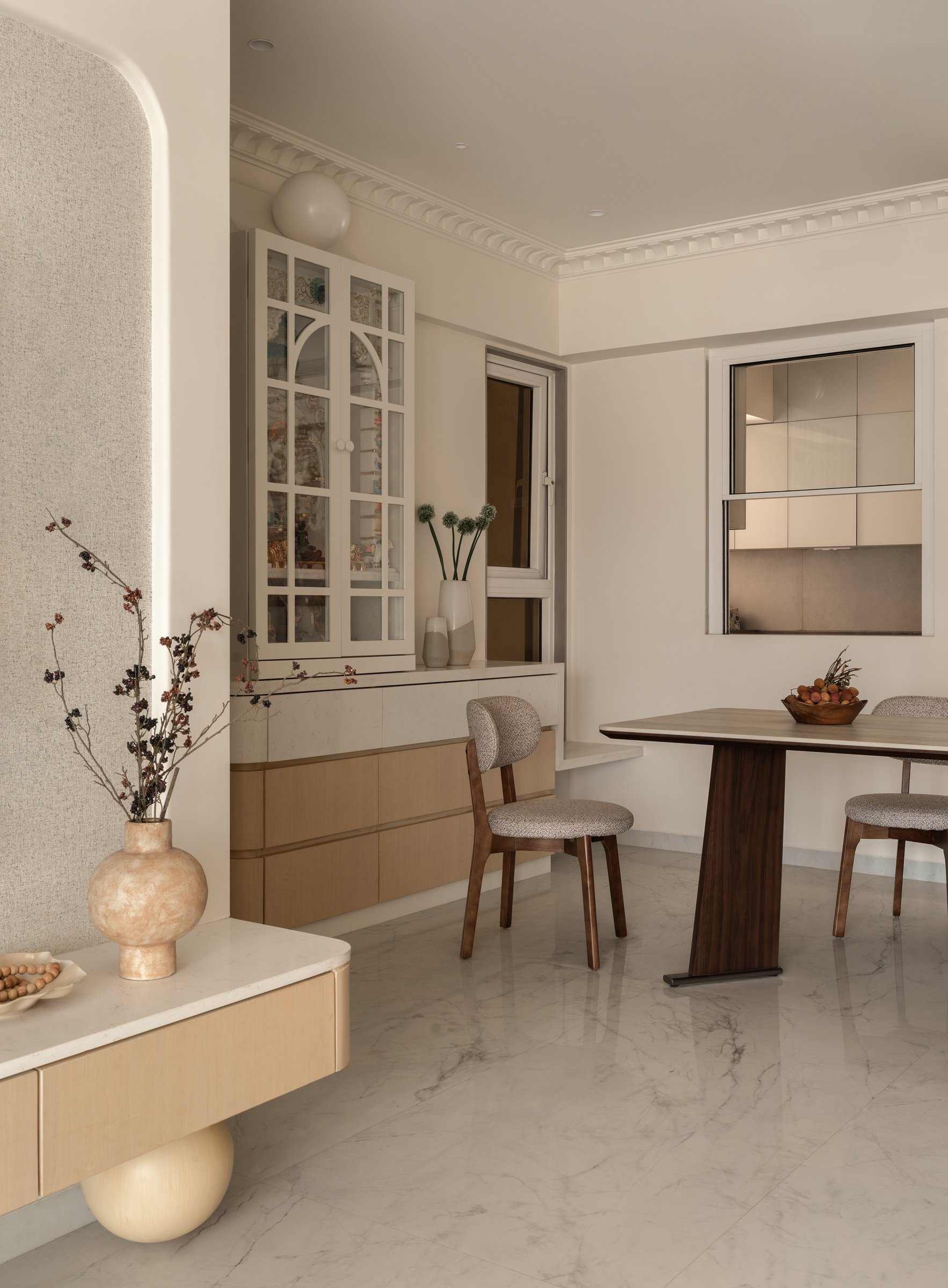 A tall glass-fronted display cabinet above blond wood cabinetry, with a service window opening into the kitchen