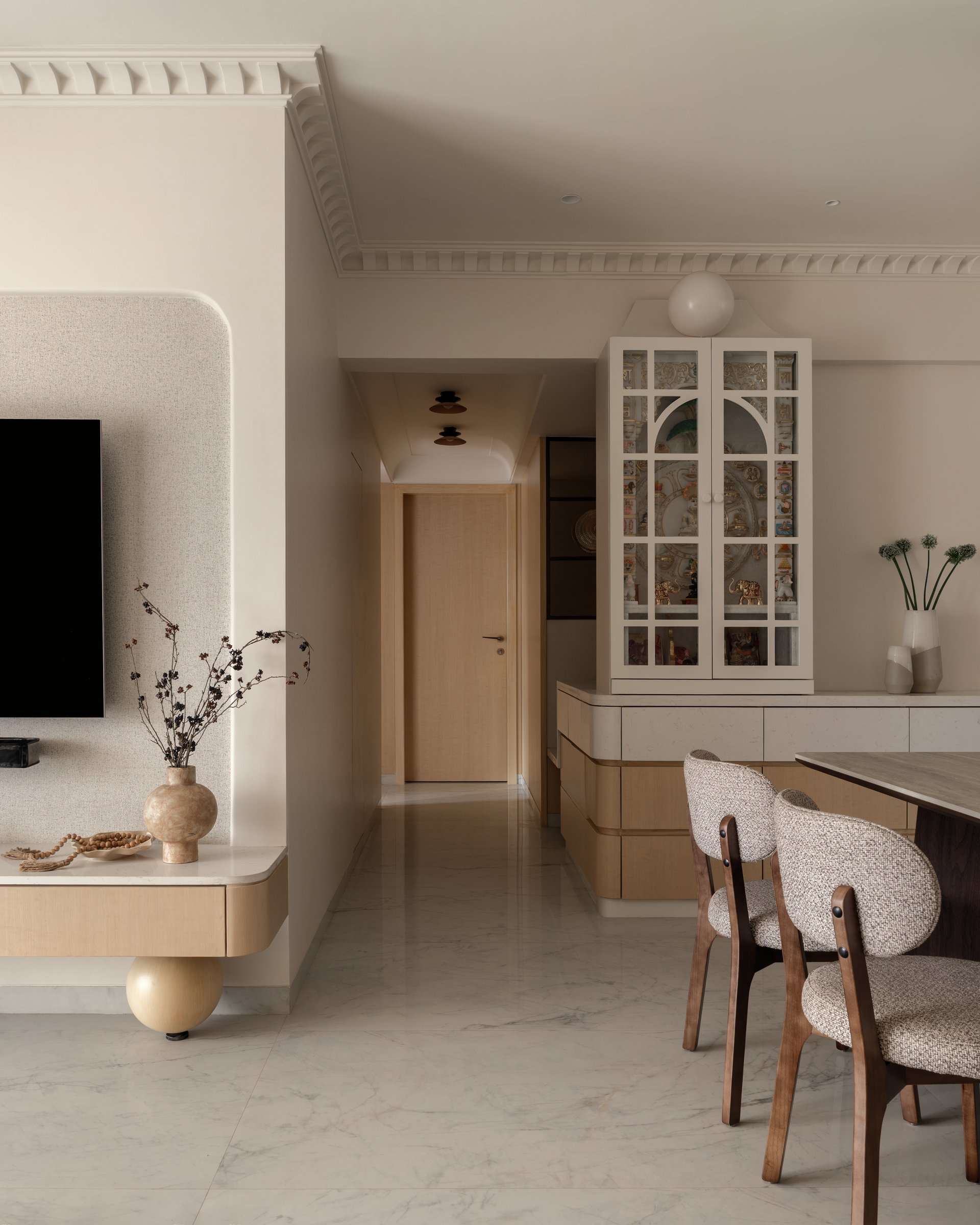 The transition from foyer into the living-and-dining volume, where blond timber joinery and a spherical-based console establish the home's material language