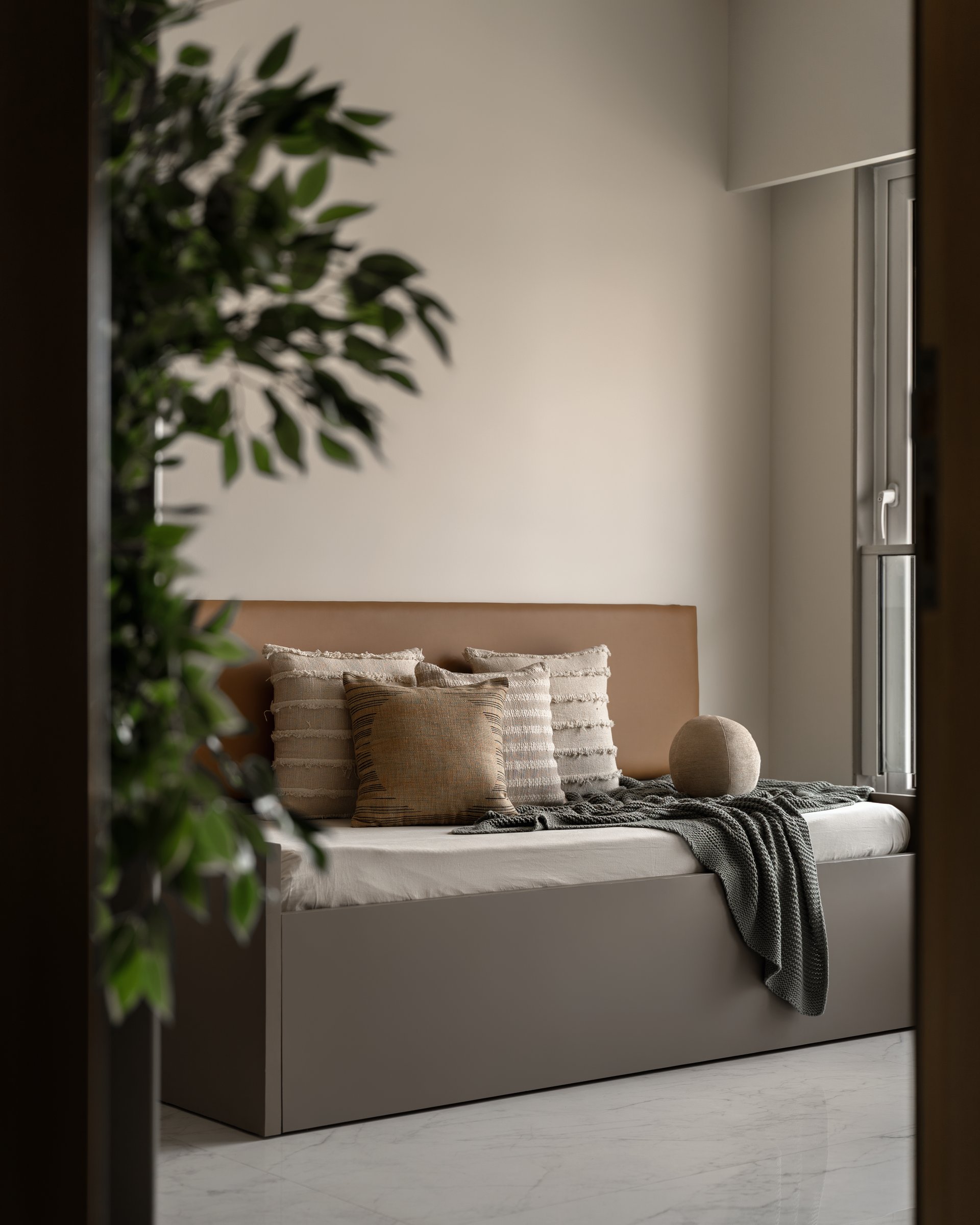 A compact daybed set beneath a window, layered with woven cushions and a textured knit throw