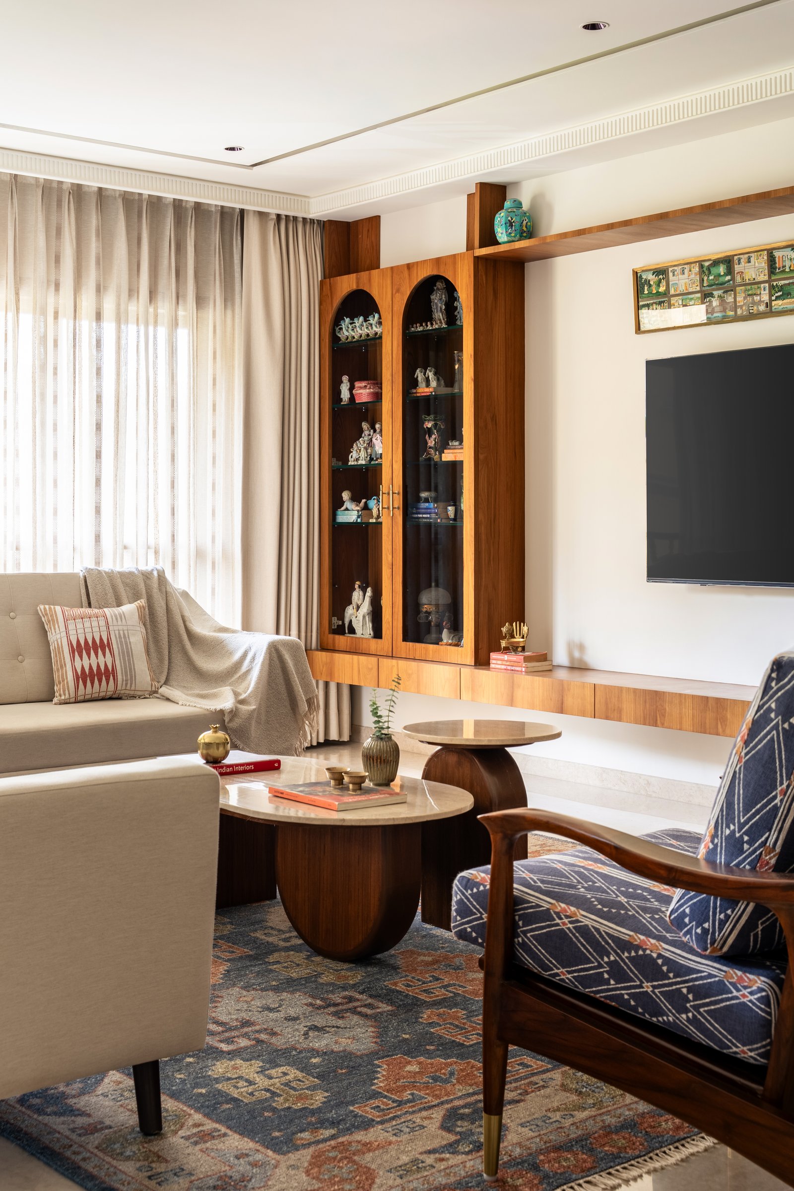 A tall timber display cabinet with arched vitrines threads collected ceramics into the living room's continuous joinery line