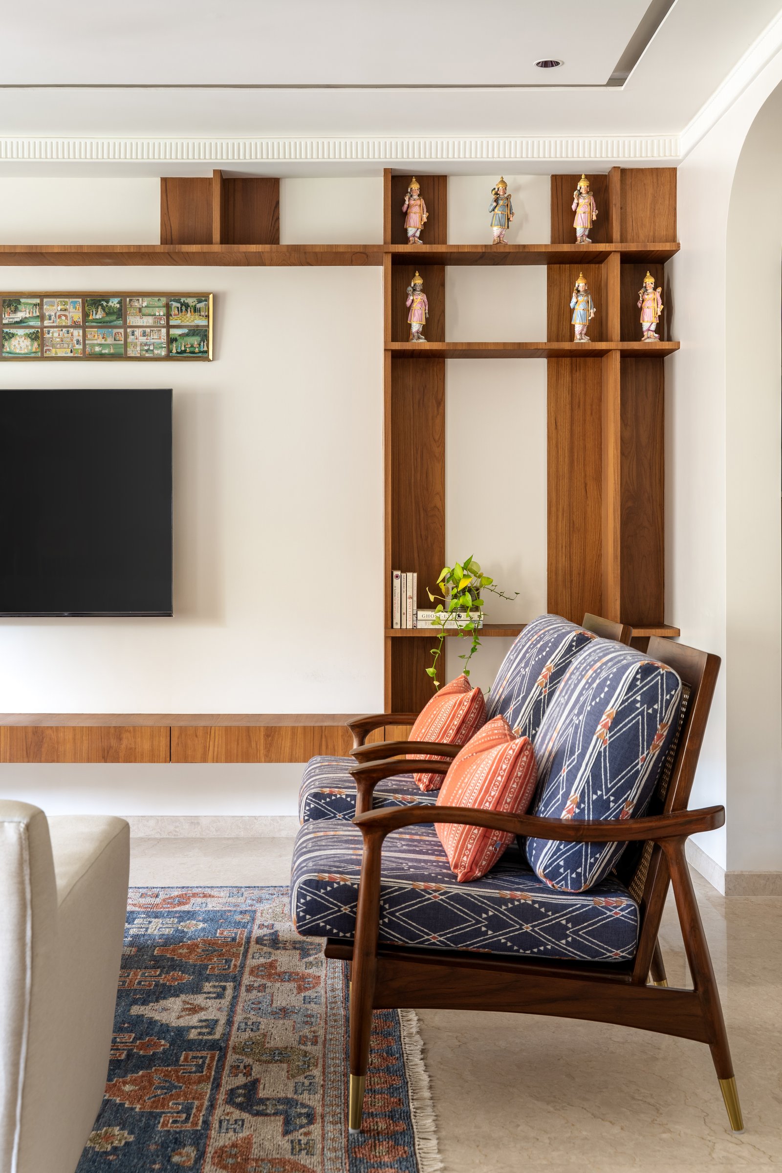 The walnut and cane armchair opposite the sofa, its patterned indigo upholstery counterpointed by open teak shelving beyond