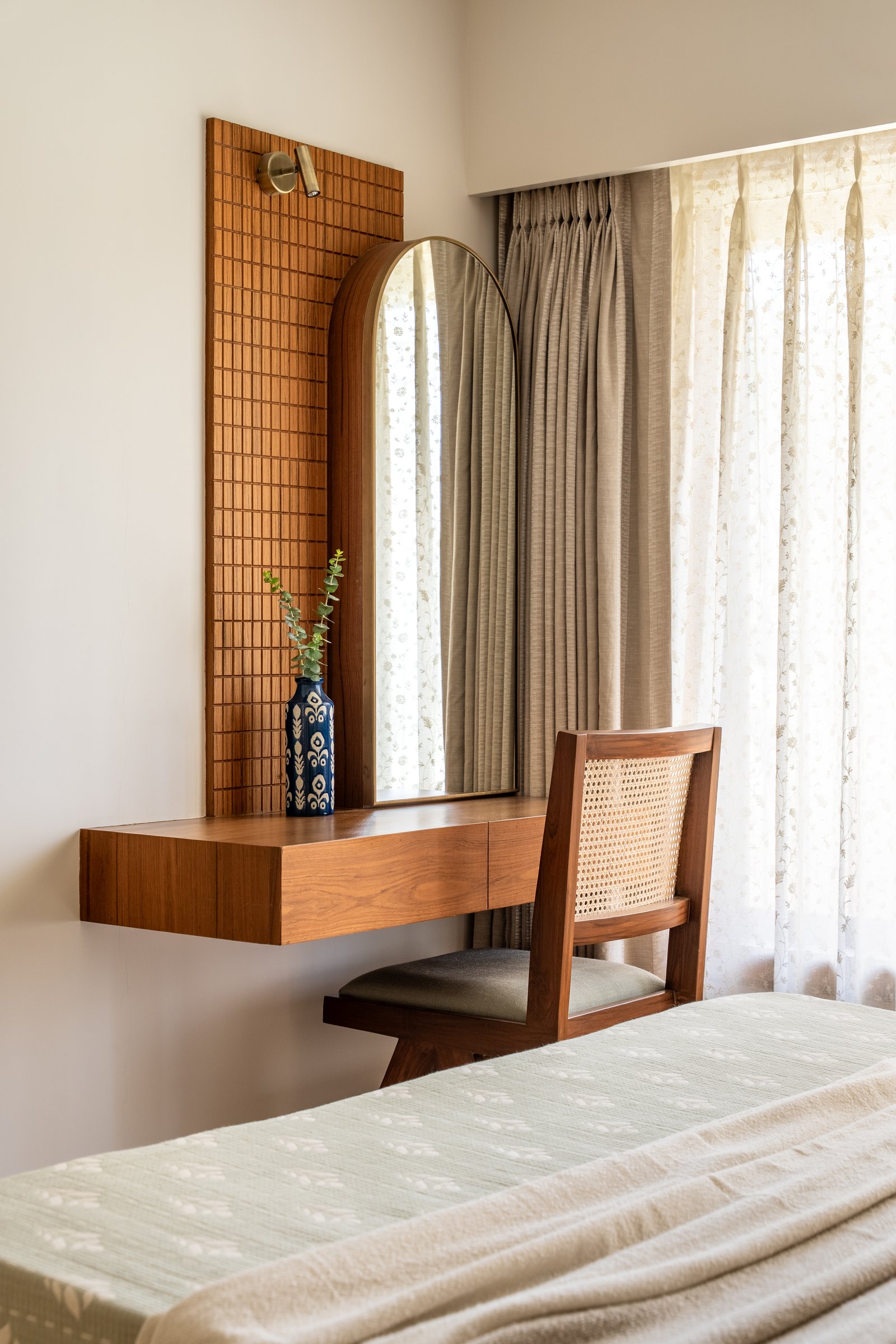 The dressing console in warm timber pairs with an arched mirror and a caned Chandigarh-style chair