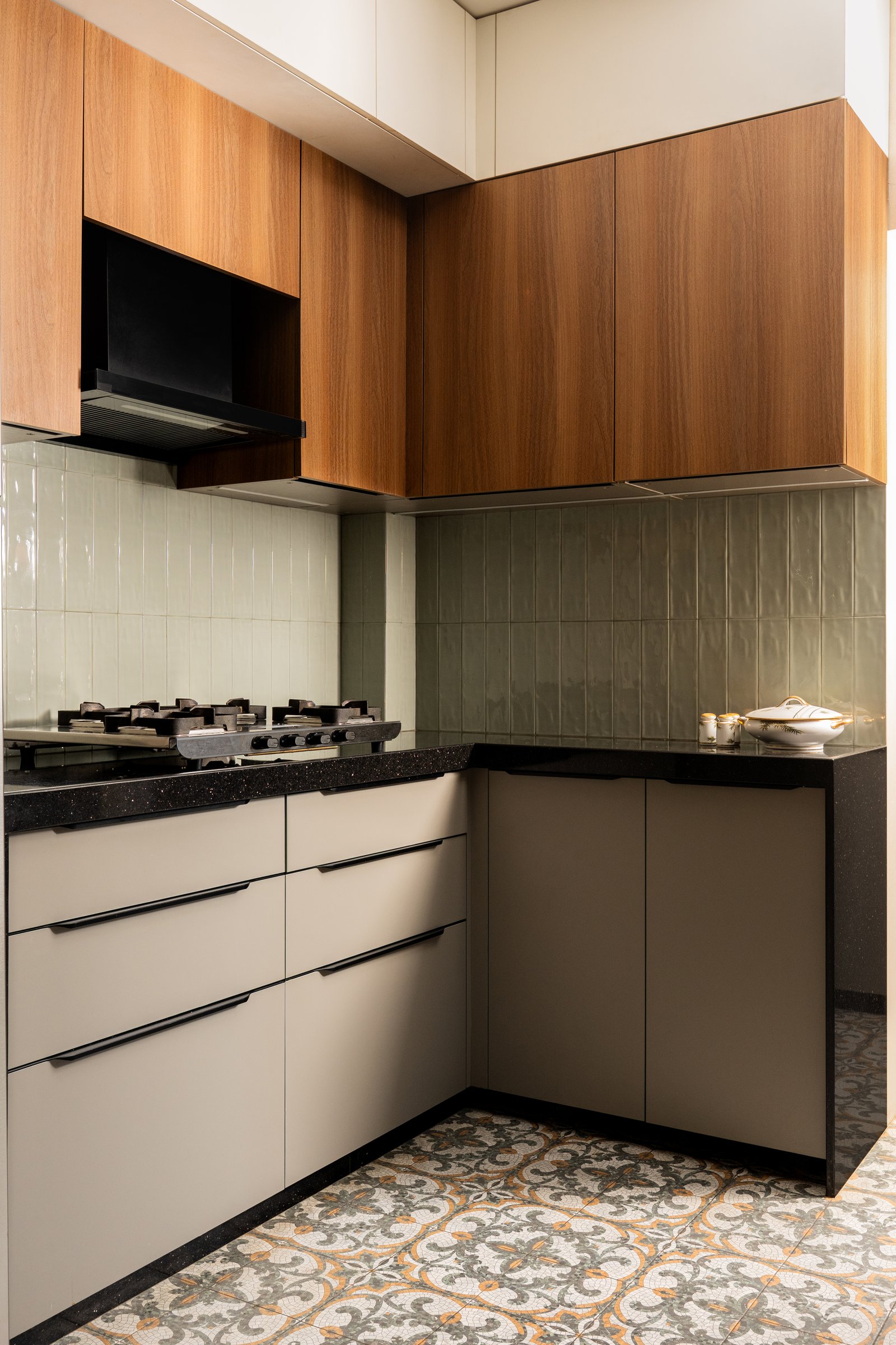 The L-shaped working corner of the kitchen, where stacked green wall tiles catch the ambient light behind a discreet black hood
