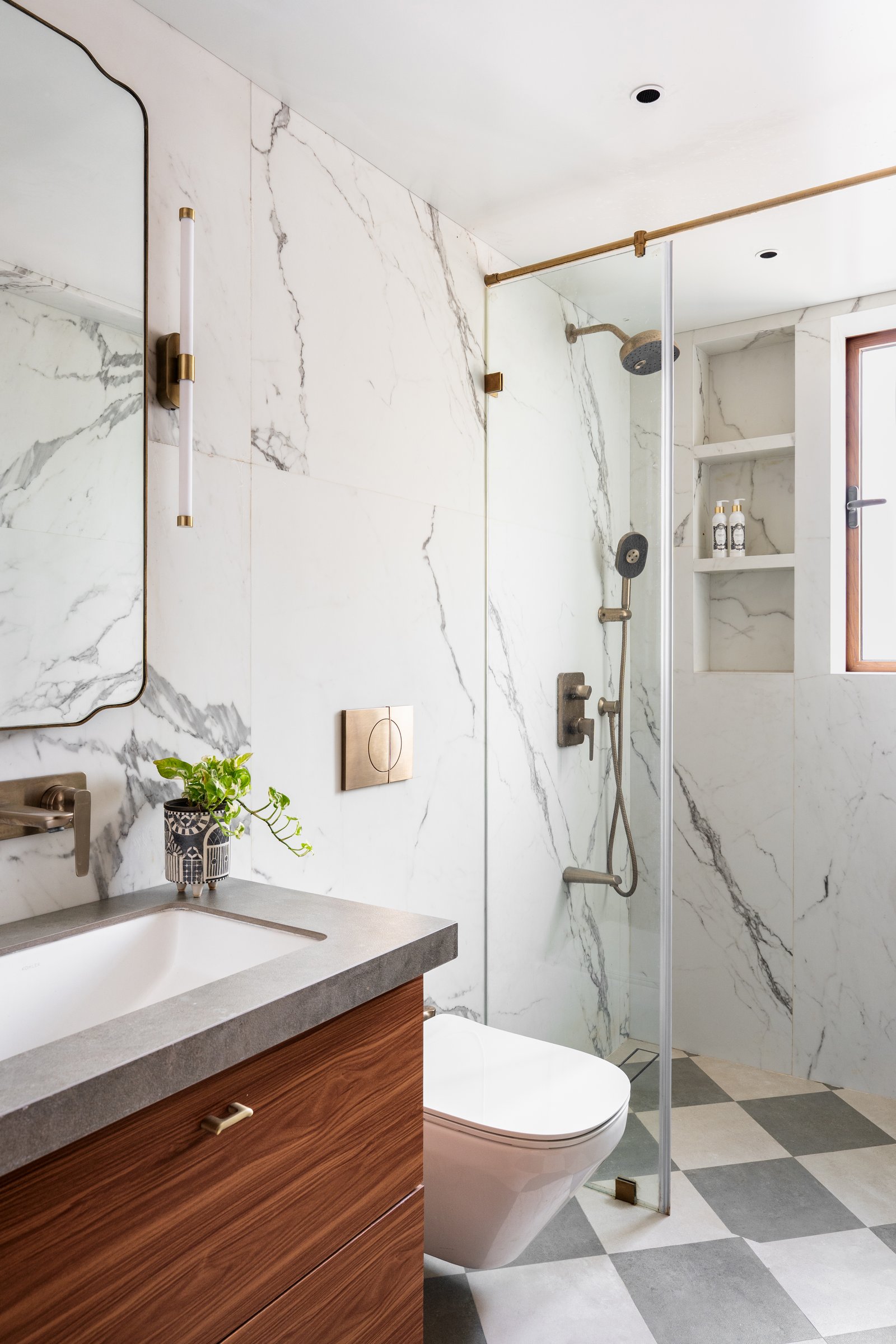 The primary bathroom, its large-format marble tempered by warm walnut cabinetry and a subtle chequerboard floor