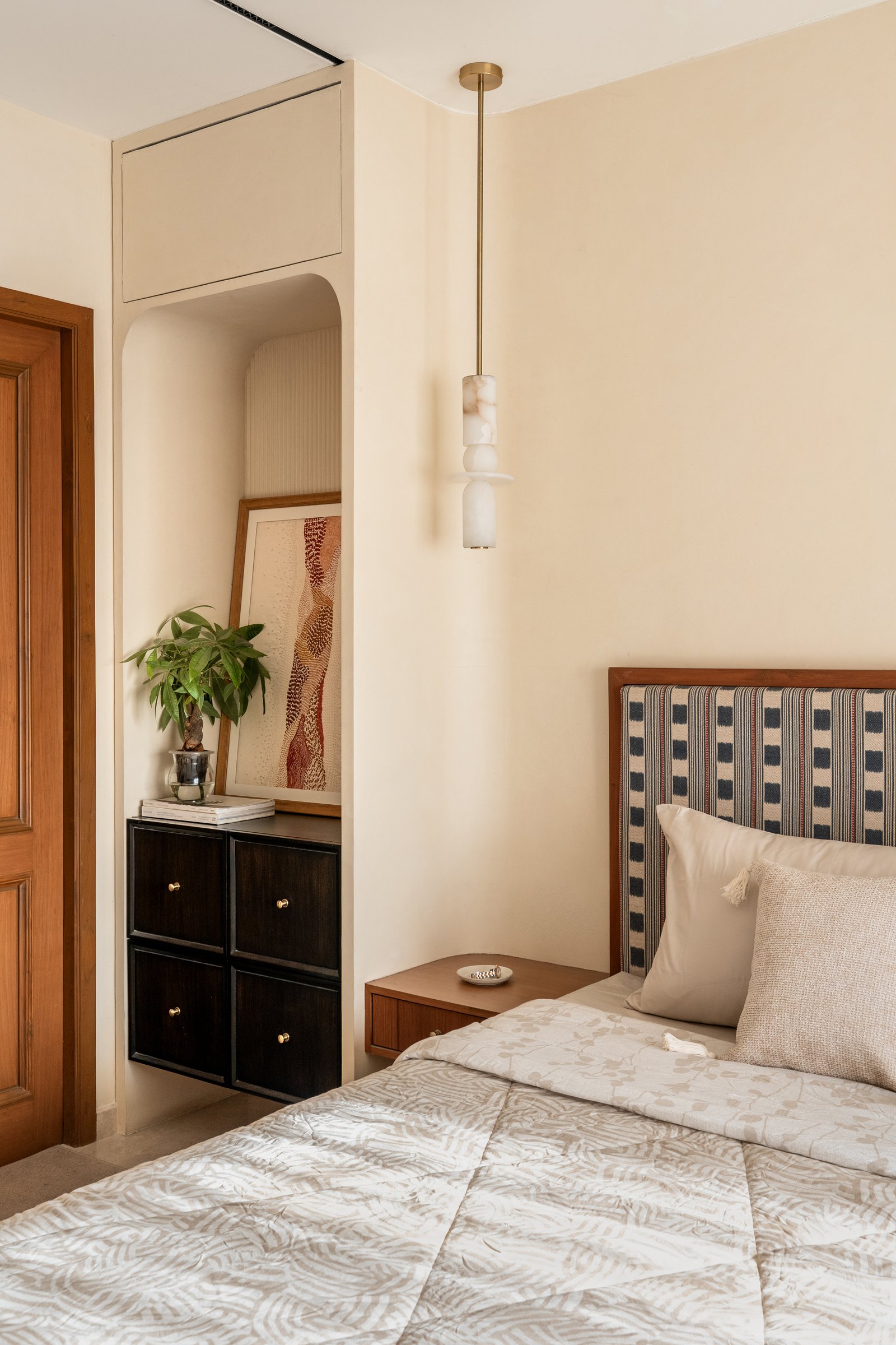 A recessed alcove with a small dark cabinet and propped artwork, framed by architecture that steps back to let objects speak