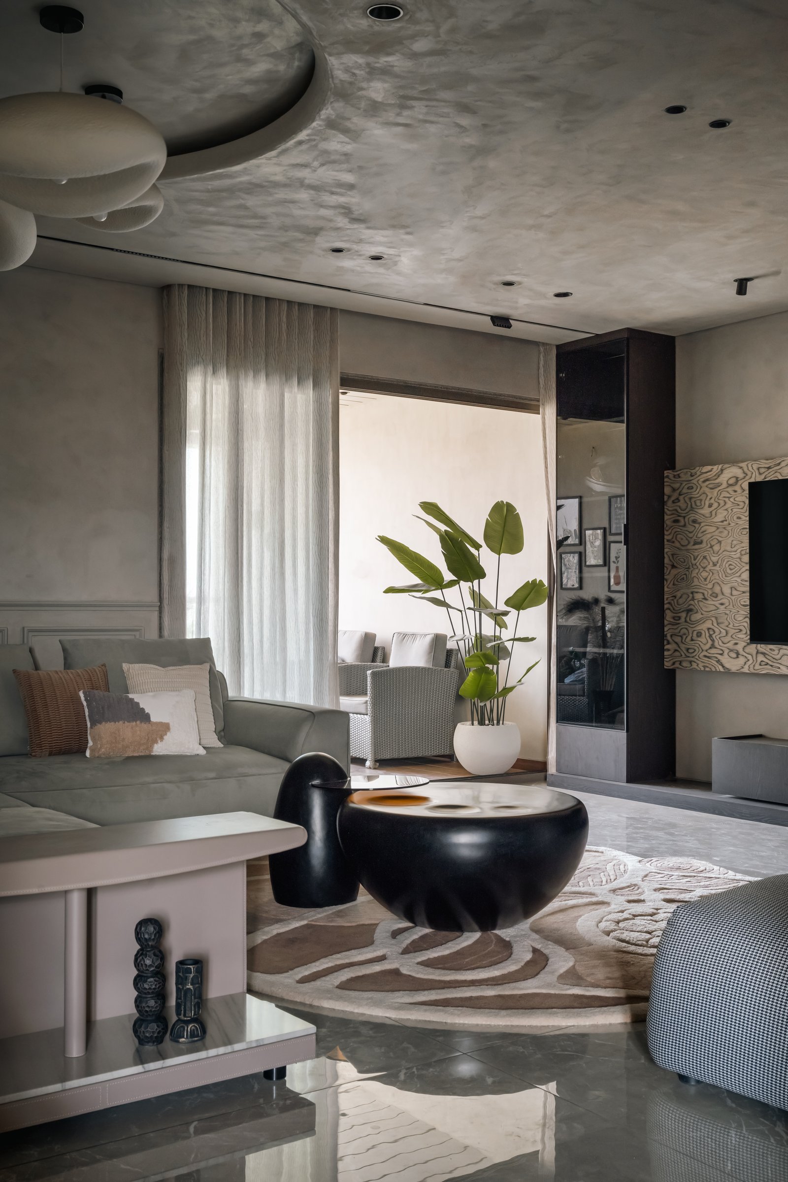 Sheer drapery filters daylight into the living room, with a potted plant marking the threshold to the lounge beyond