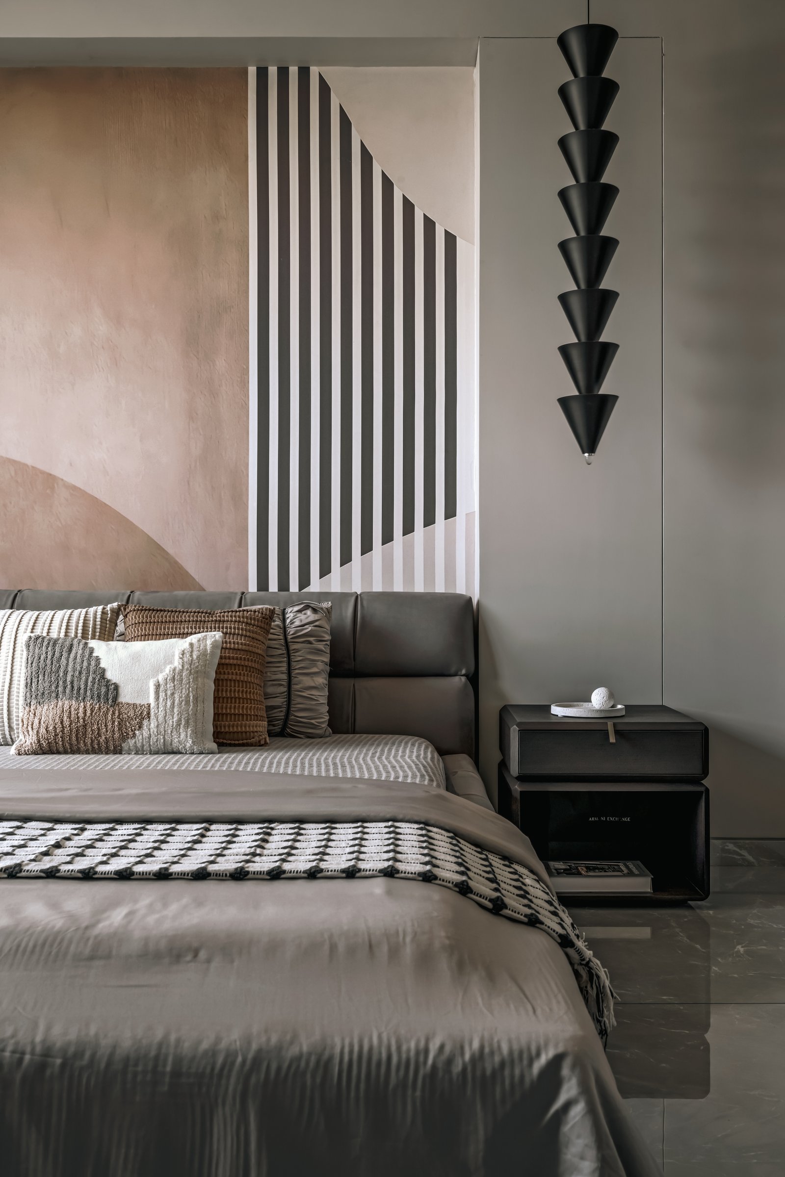 A slim sculptural pendant of stacked matte-black cones hangs beside the bed