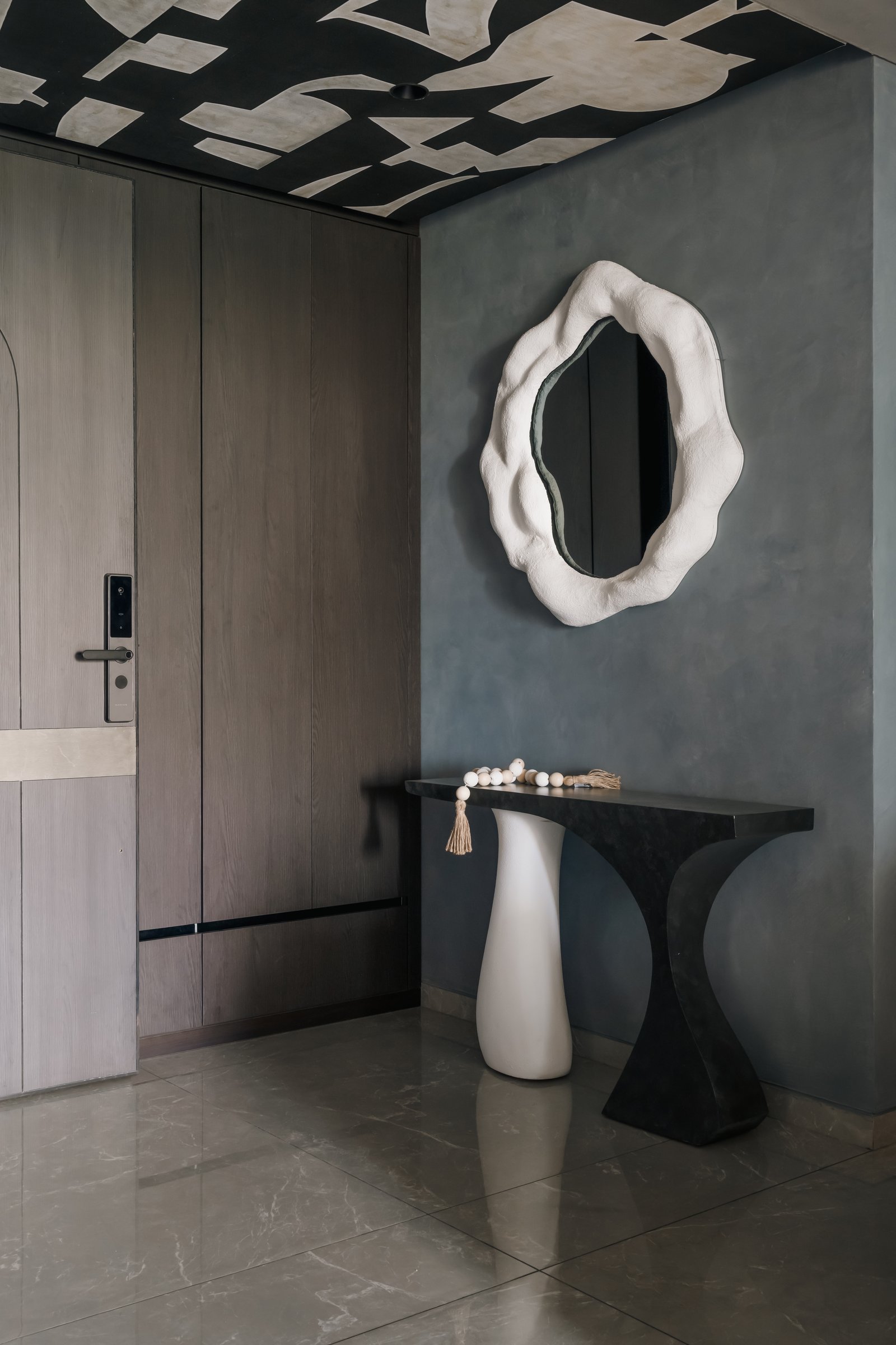 The foyer, where a sculptural console and an organically shaped mirror sit beneath an abstract ceiling mural