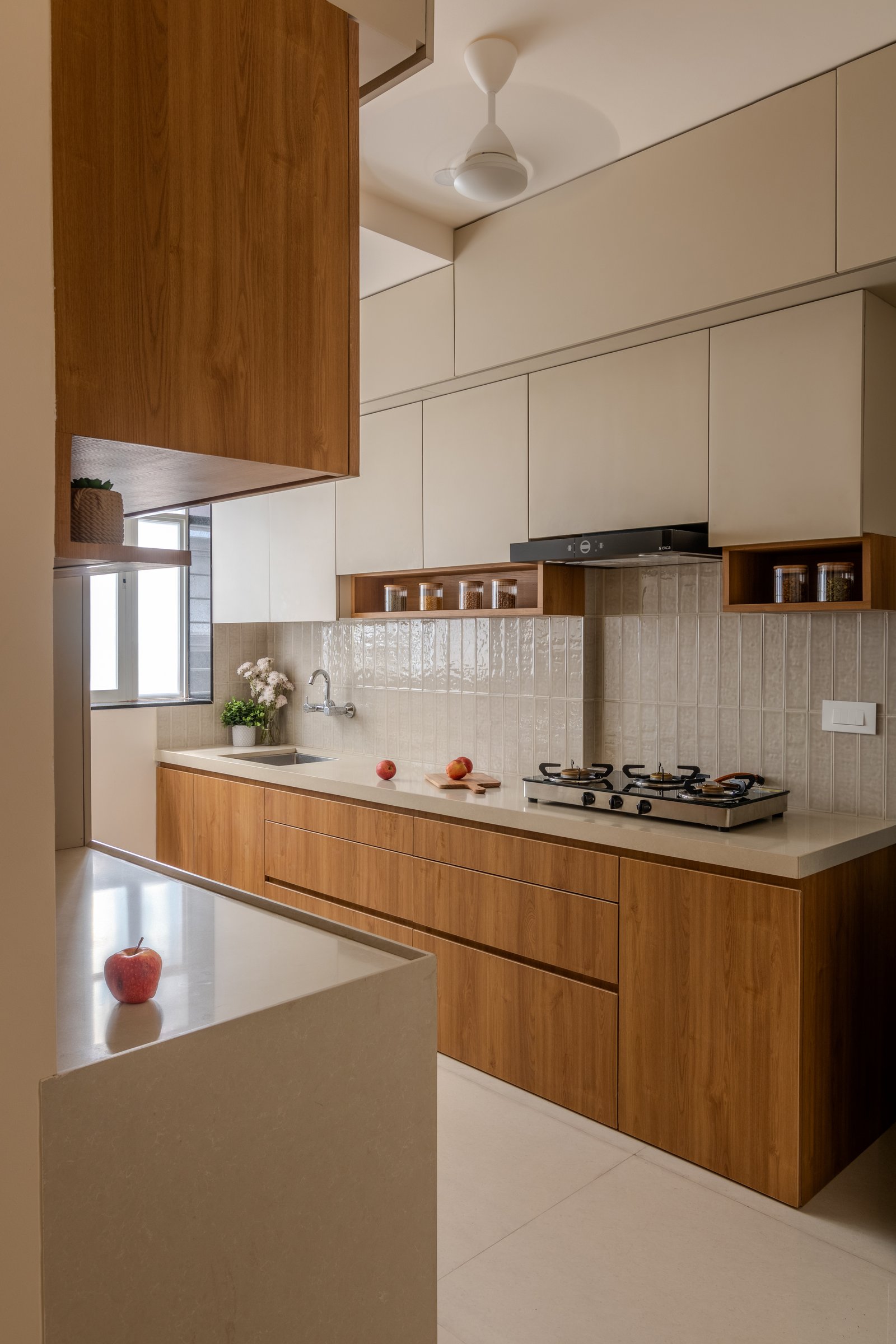 The kitchen, where warm wooden base cabinetry meets tall pale upper units for maximum storage