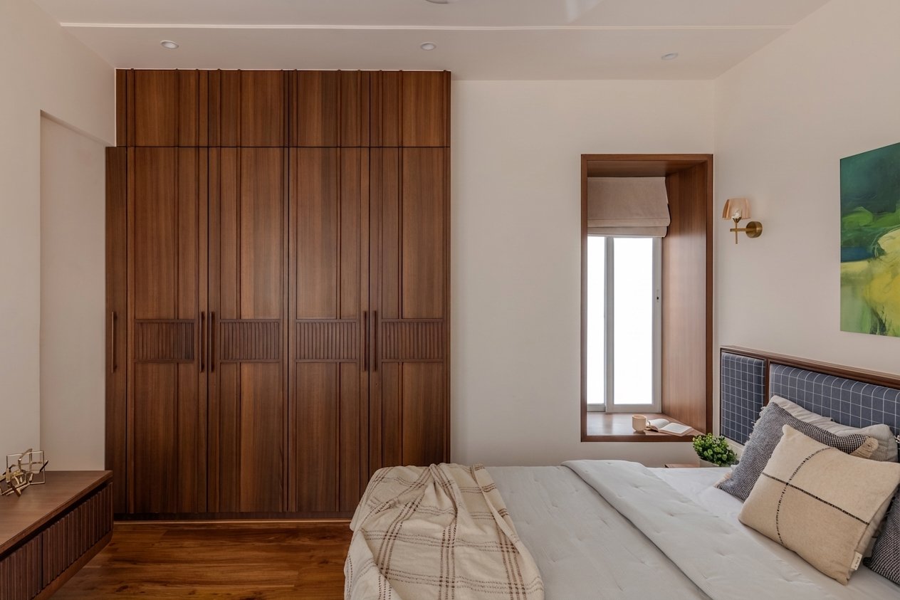 The full-height veneered wardrobe opposite the bed, its grooved handle detail echoing the dining chairs