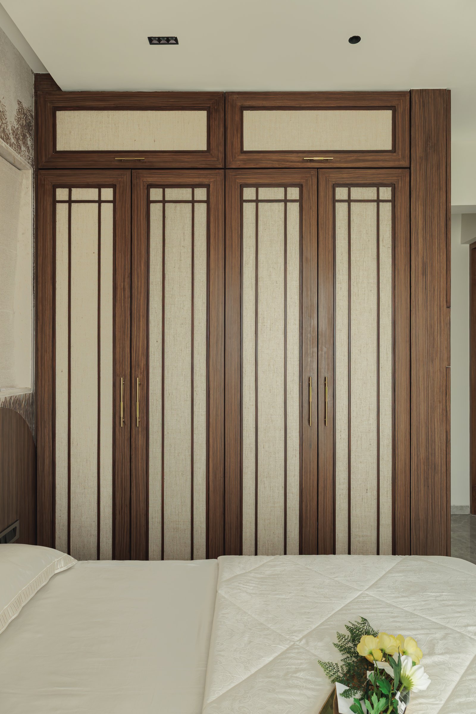 The wardrobe wall of the second bedroom, with tall walnut doors paneled in woven fabric and slim brass detailing