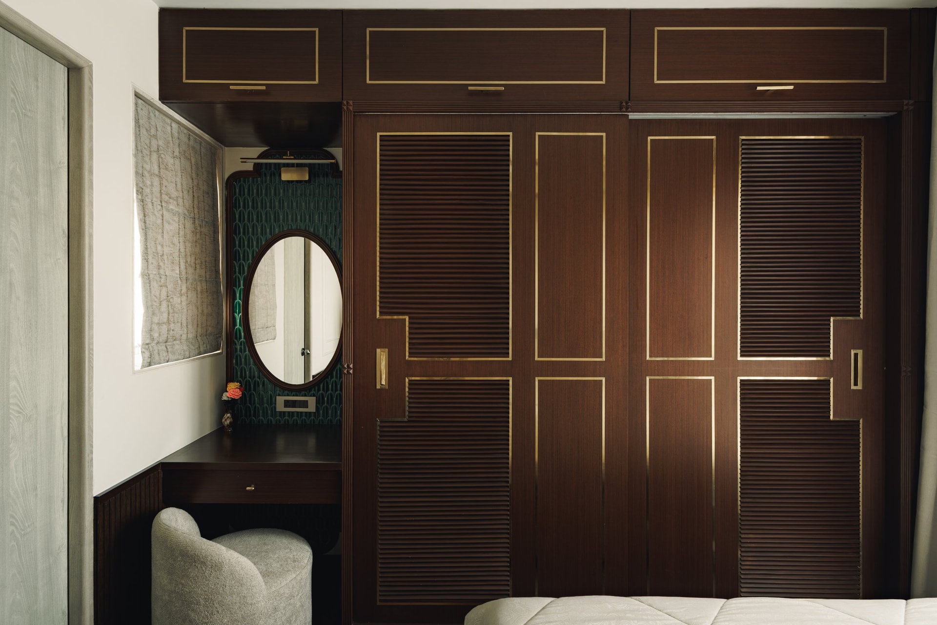 The dressing joinery, where louvred timber doors with brass inlay meet an oval-mirrored vanity backed by green patterned wallpaper