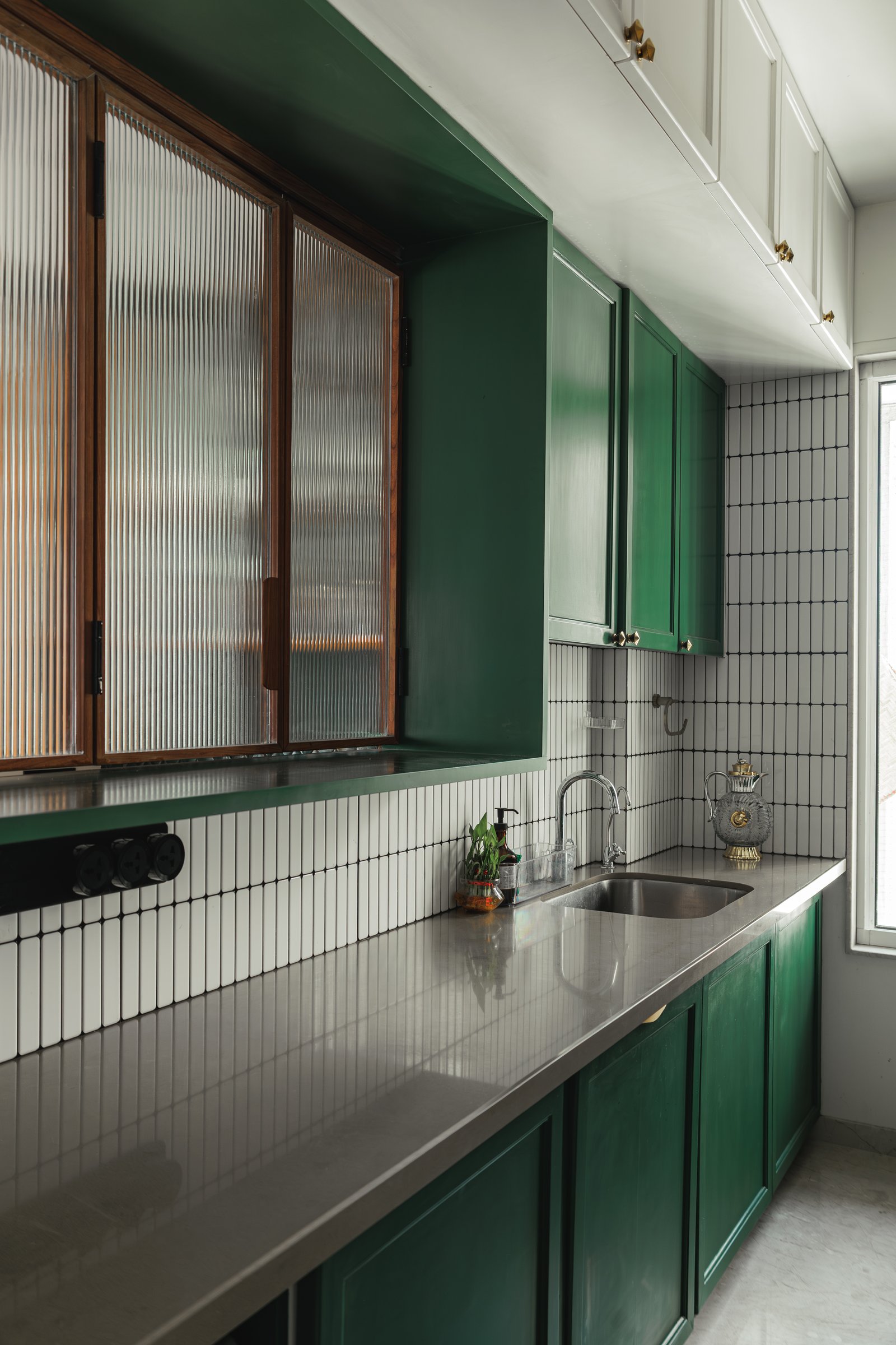 The kitchen, where emerald green cabinetry meets a graphic backsplash of narrow white tiles in black grout