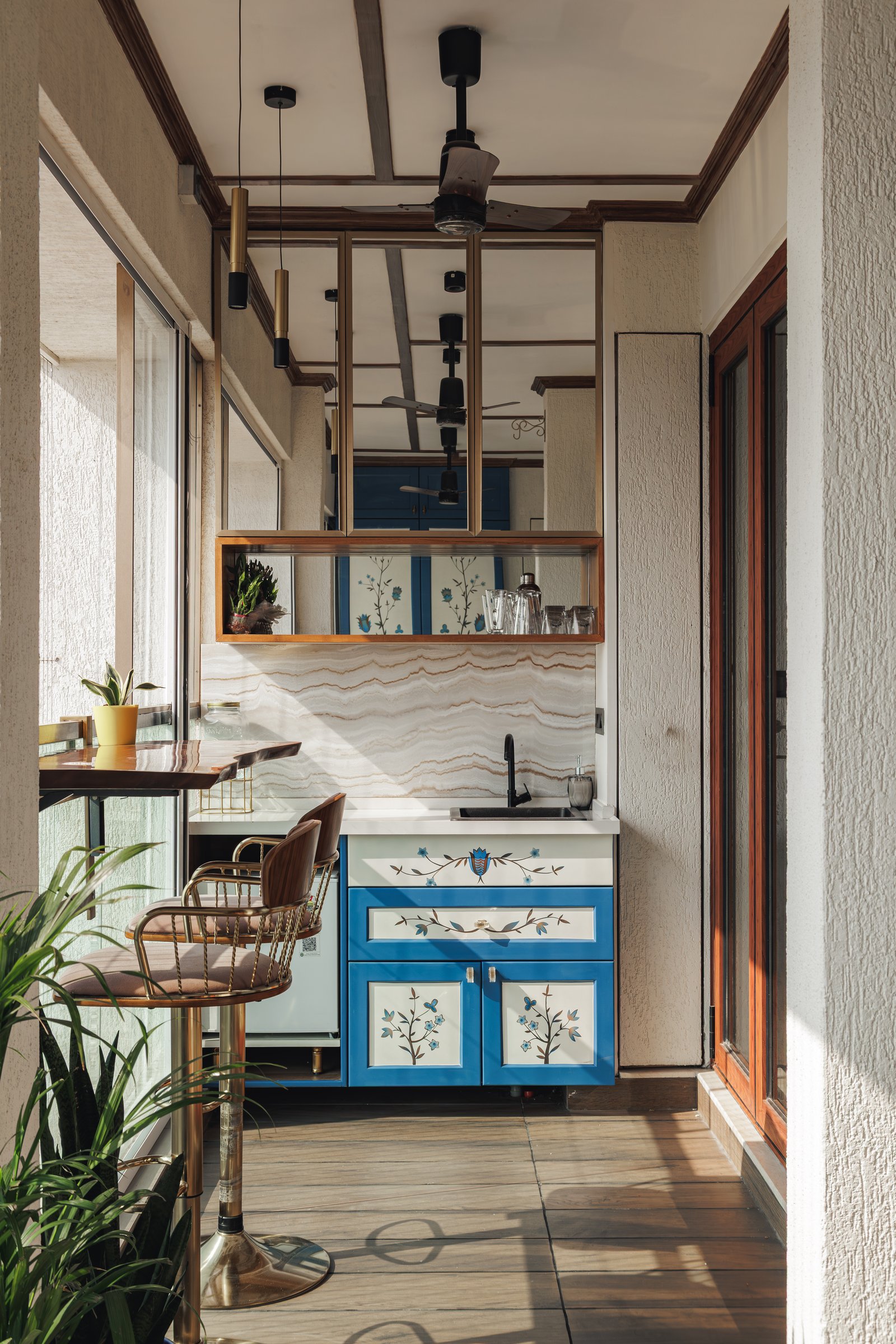 The balcony bar, where blue floral cabinetry meets a swirling marble backsplash and a metal-and-mirror shelf