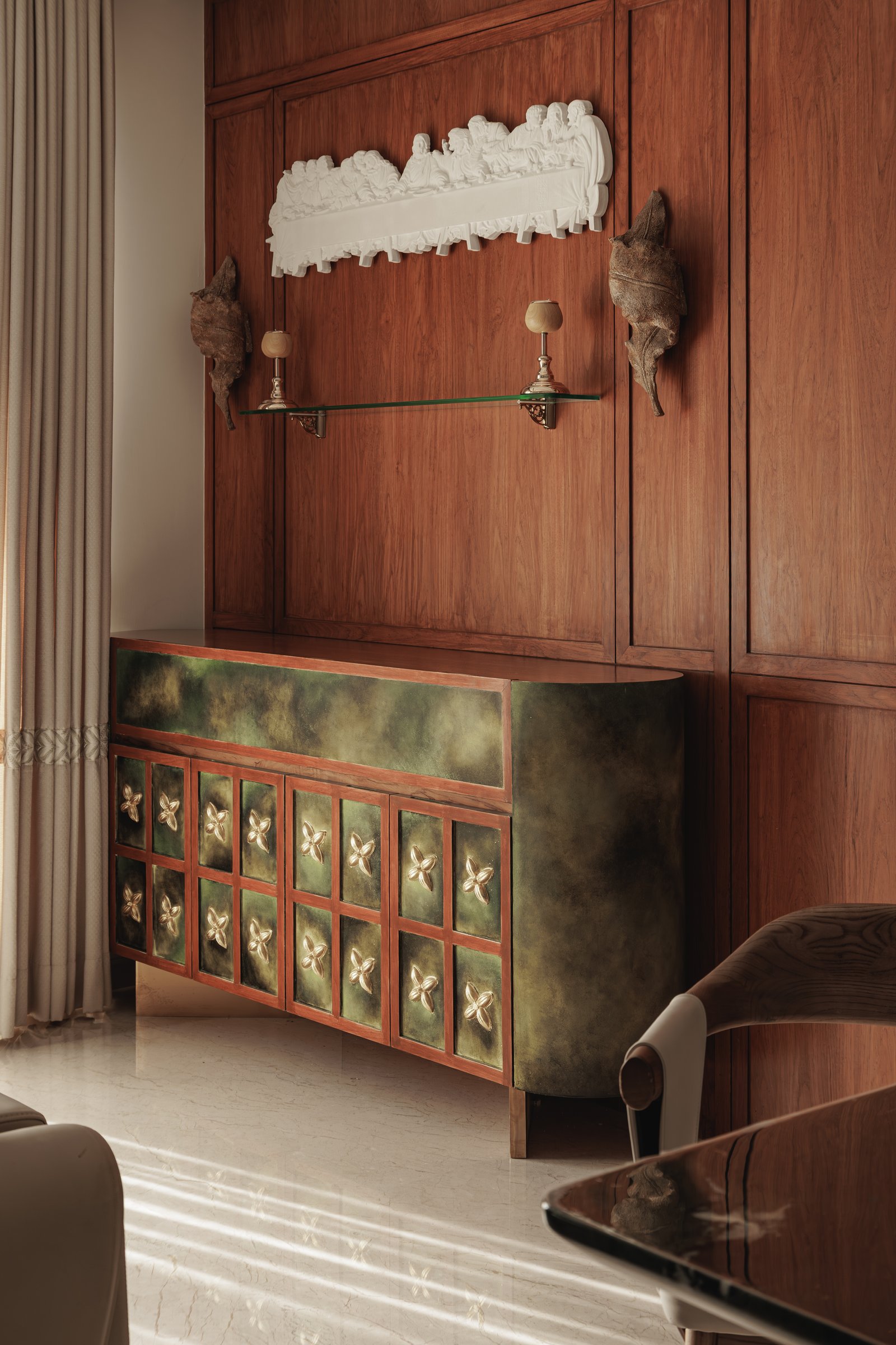 The dining zone, where a mossy green curved sideboard with copper-framed floral panels anchors the walnut-lined wall