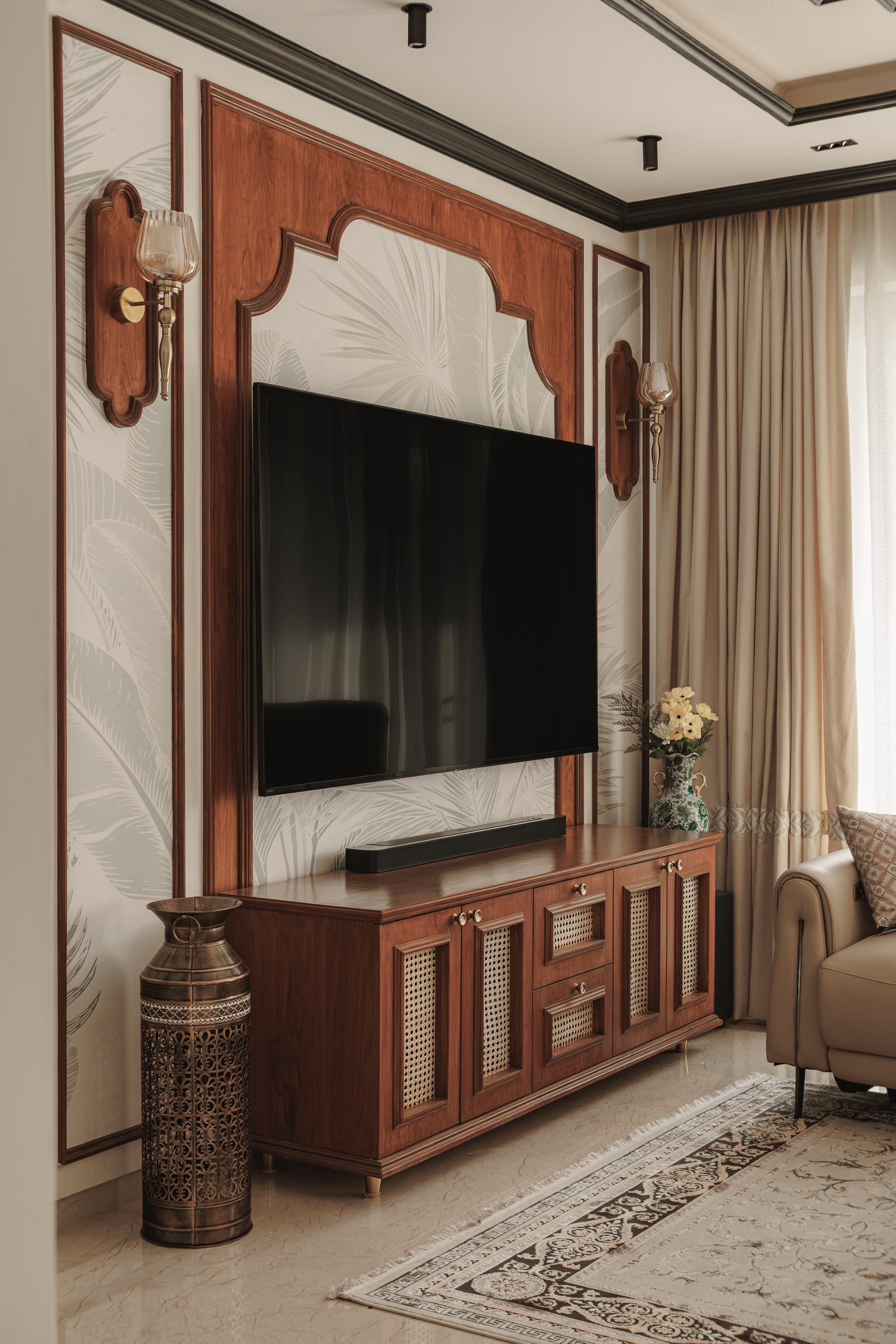 The media console: a cane-fronted walnut sideboard set against pale palm-frond wallpaper and flanked by brass sconces
