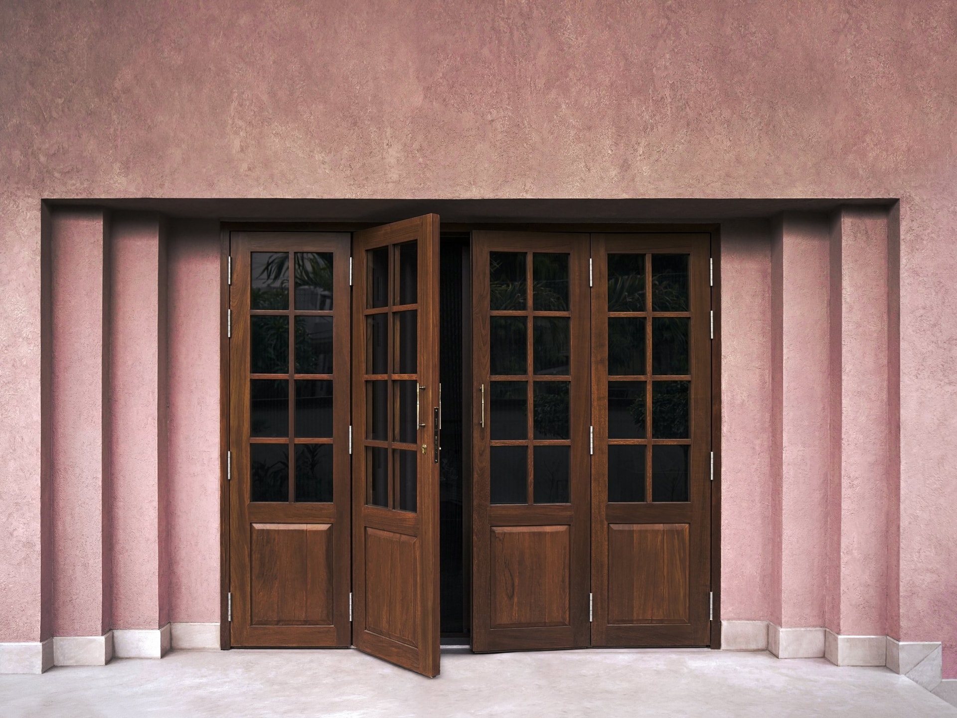 The reworked exterior, set in warm rose-pink plaster with paired timber-and-glass entry doors