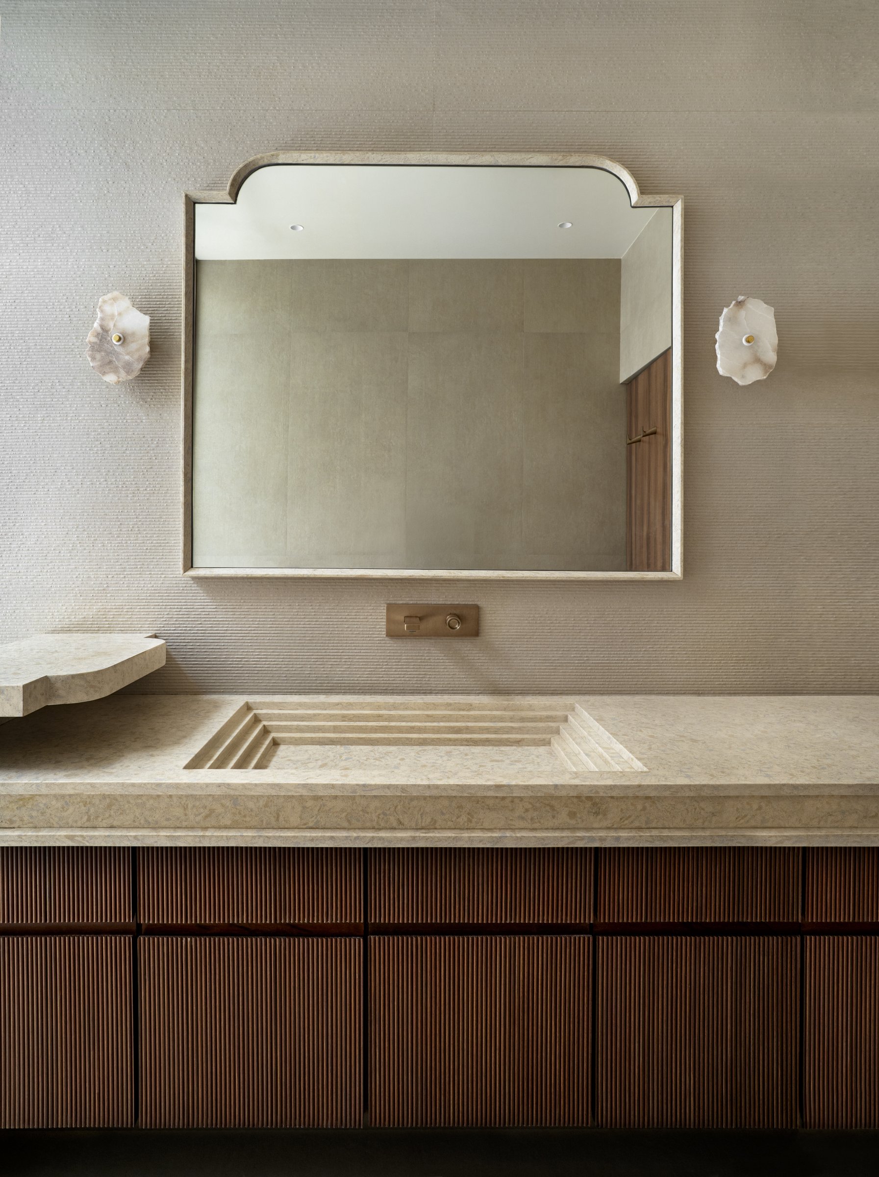 The primary bathroom, where a custom stone counter with a stepped recessed basin sits above a fluted timber vanity