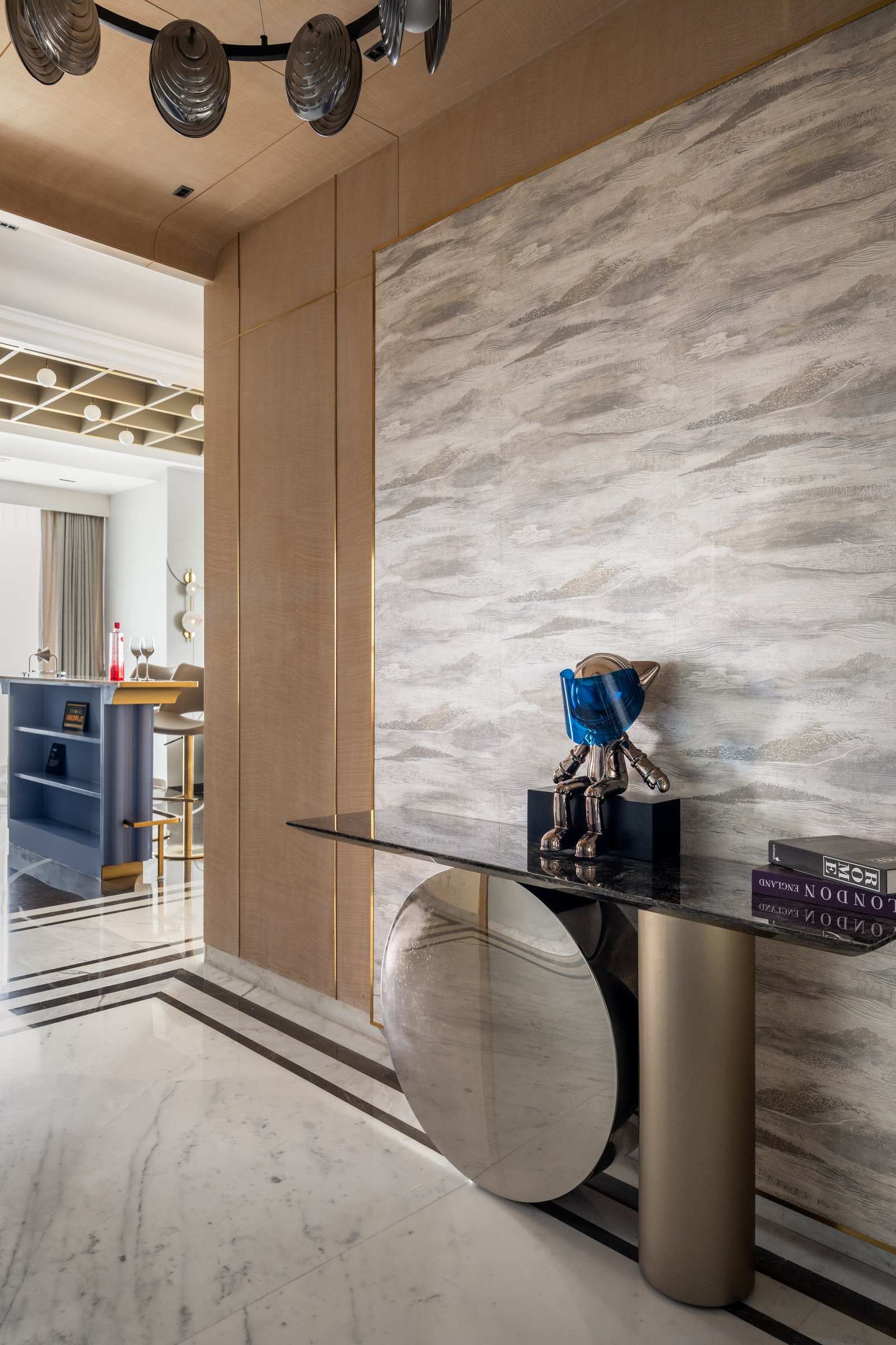 The foyer, where a textured wall covering, a brass-and-marble console and a sculptural chandelier introduce the home's softened Deco vocabulary