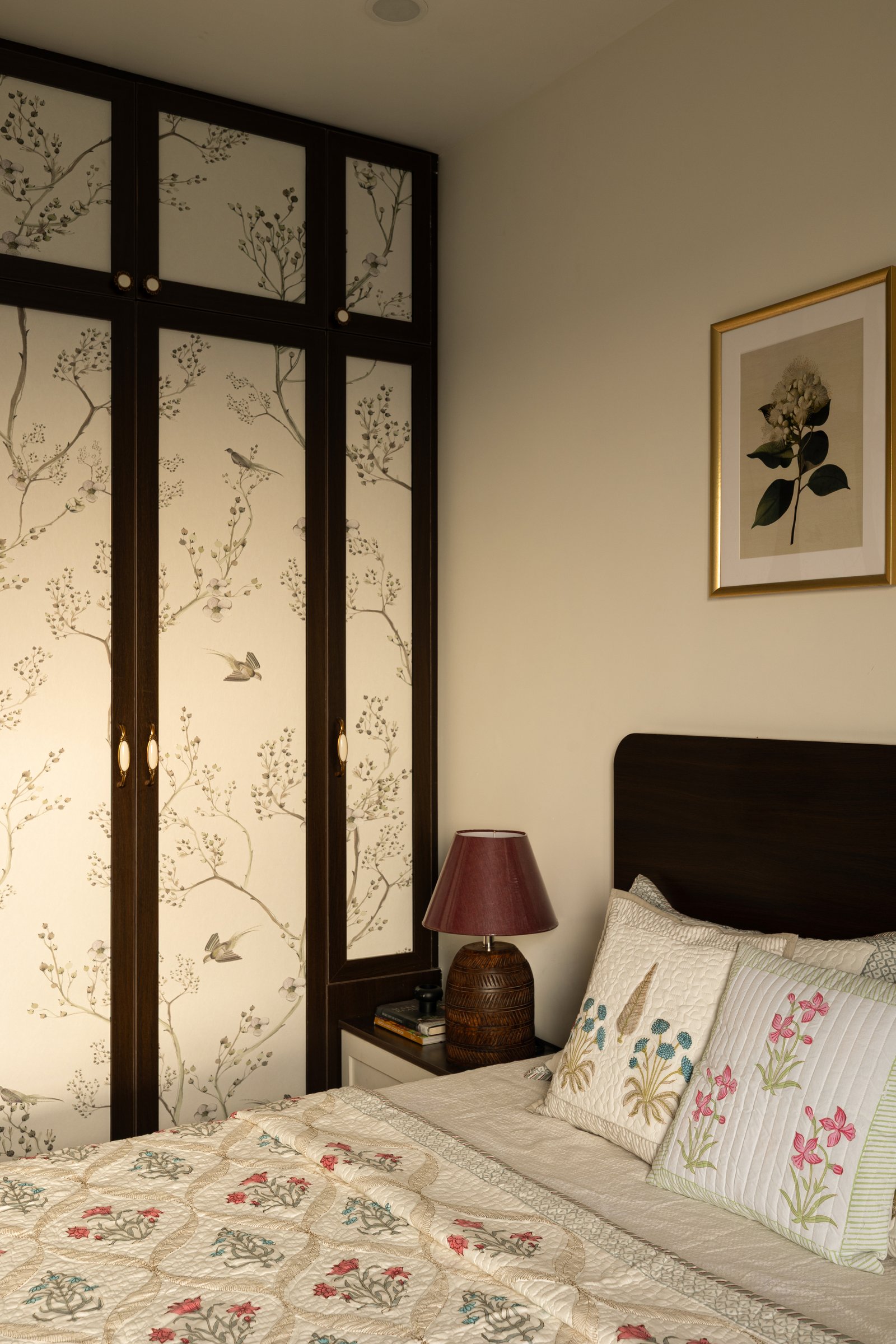 The built-in wardrobe, framed in dark wood around panels of botanical wallpaper so storage reads as decorative surface