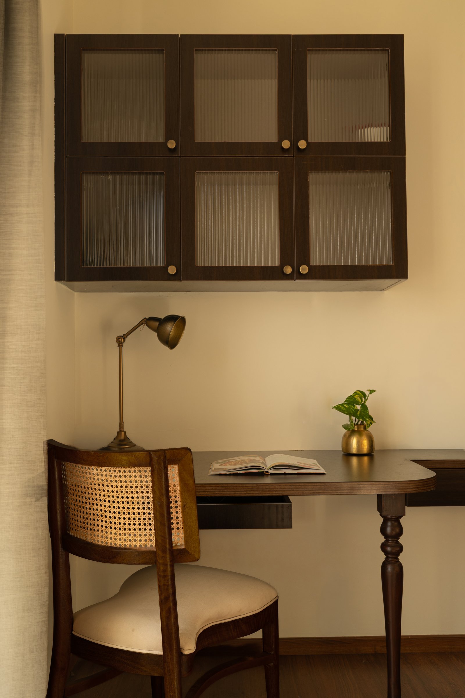 A study nook within the bedroom, where a cane-backed chair and reeded-glass cabinetry carry the home's language into its quietest corner
