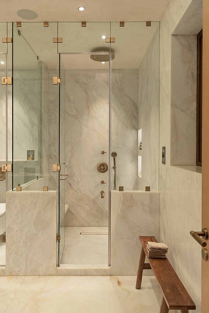 The marble-clad shower, enclosed in brass-framed glass with a small wooden bench alongside
