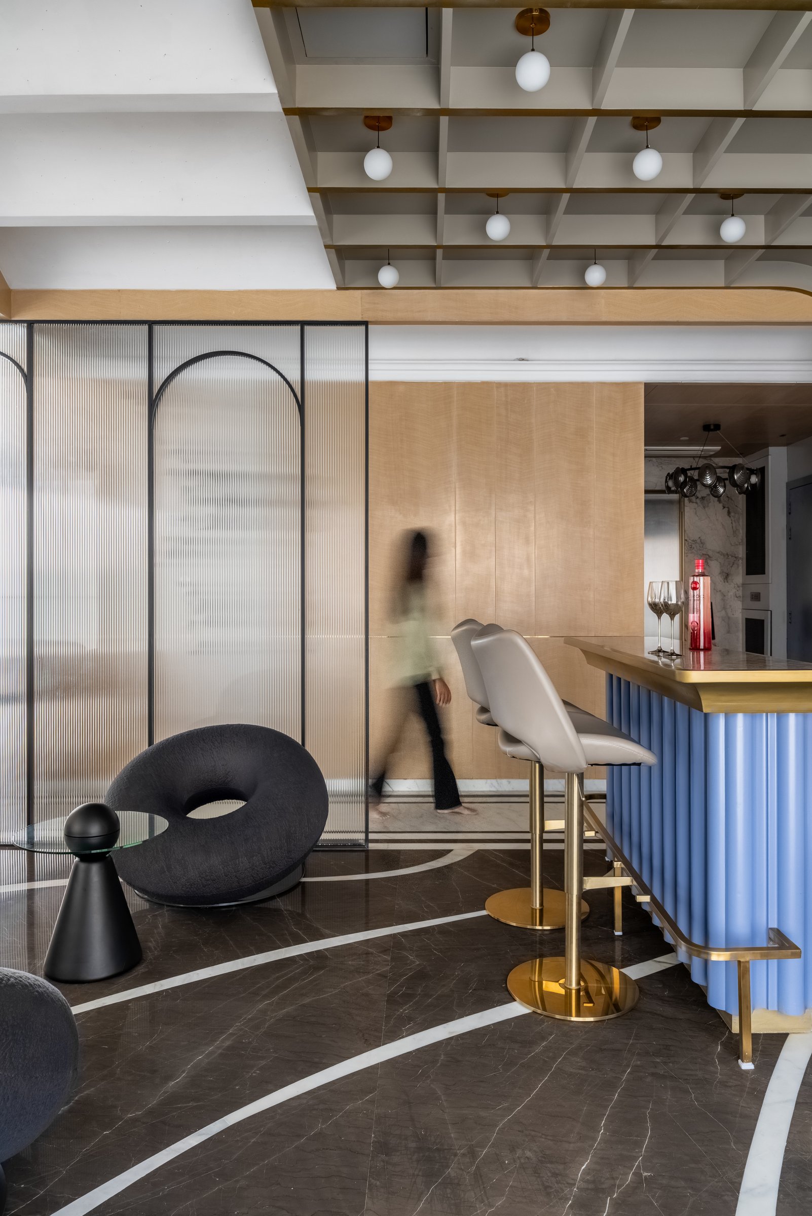 The lounge beside the bar, where a dark inlaid stone floor and a reeded glass screen frame a sculptural ring-shaped chair