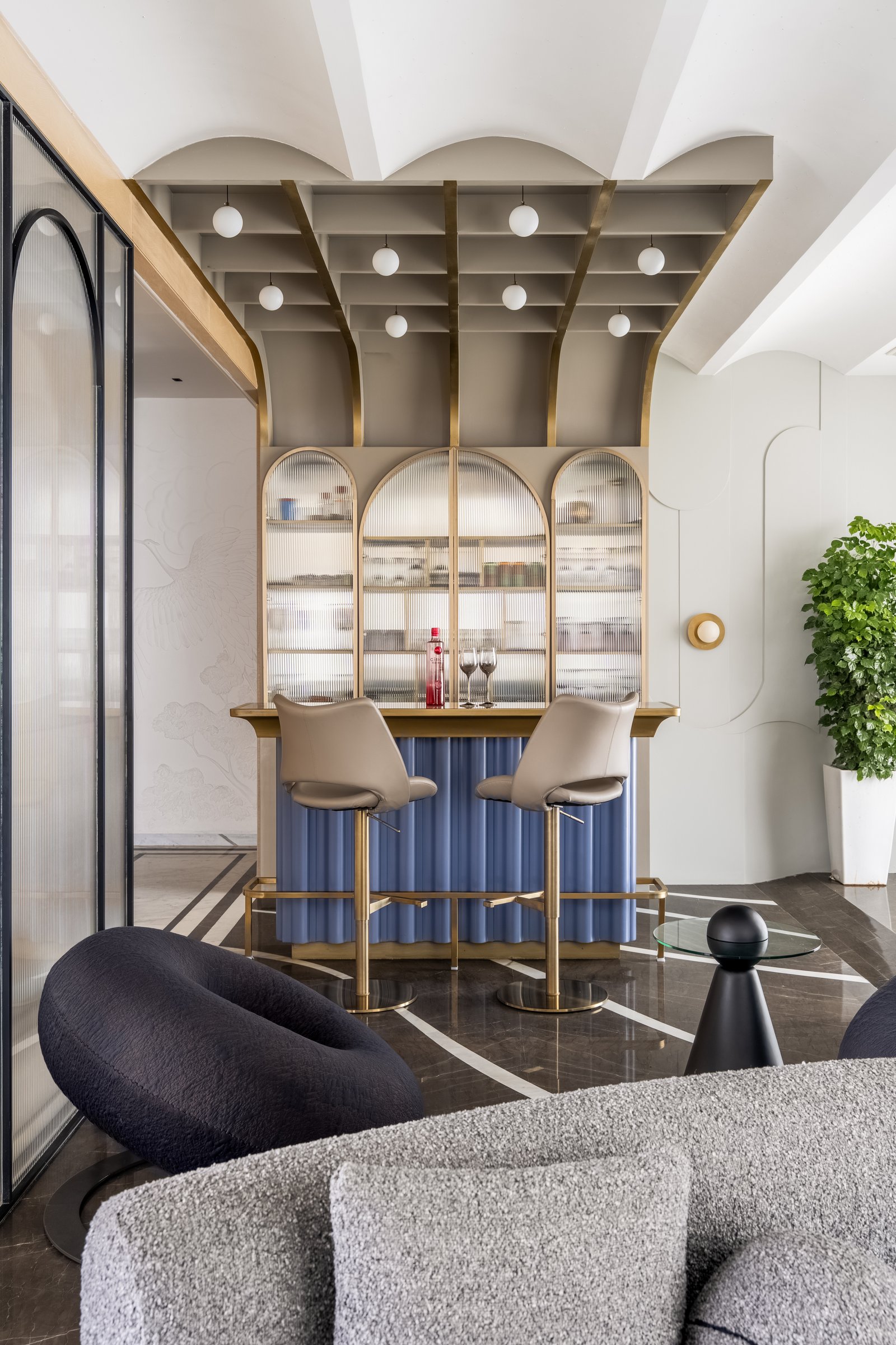 The bar, with arched reeded-glass cabinets, a periwinkle fluted counter and a brass-coffered ceiling of opal globe pendants