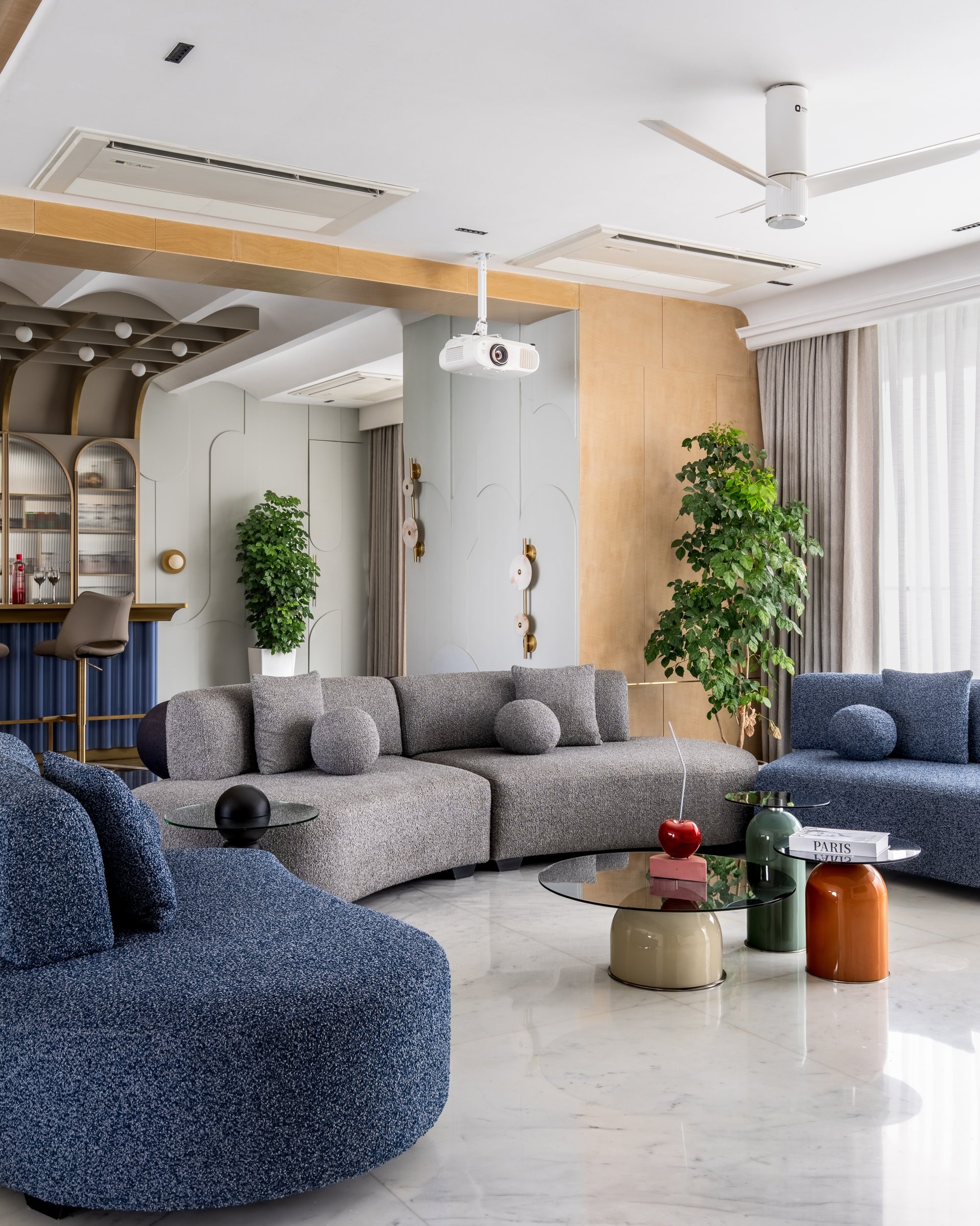 The living room, where a curved grey bouclé sectional and blue bouclé armchairs sit against sculpted wall panelling and warm veneered joinery