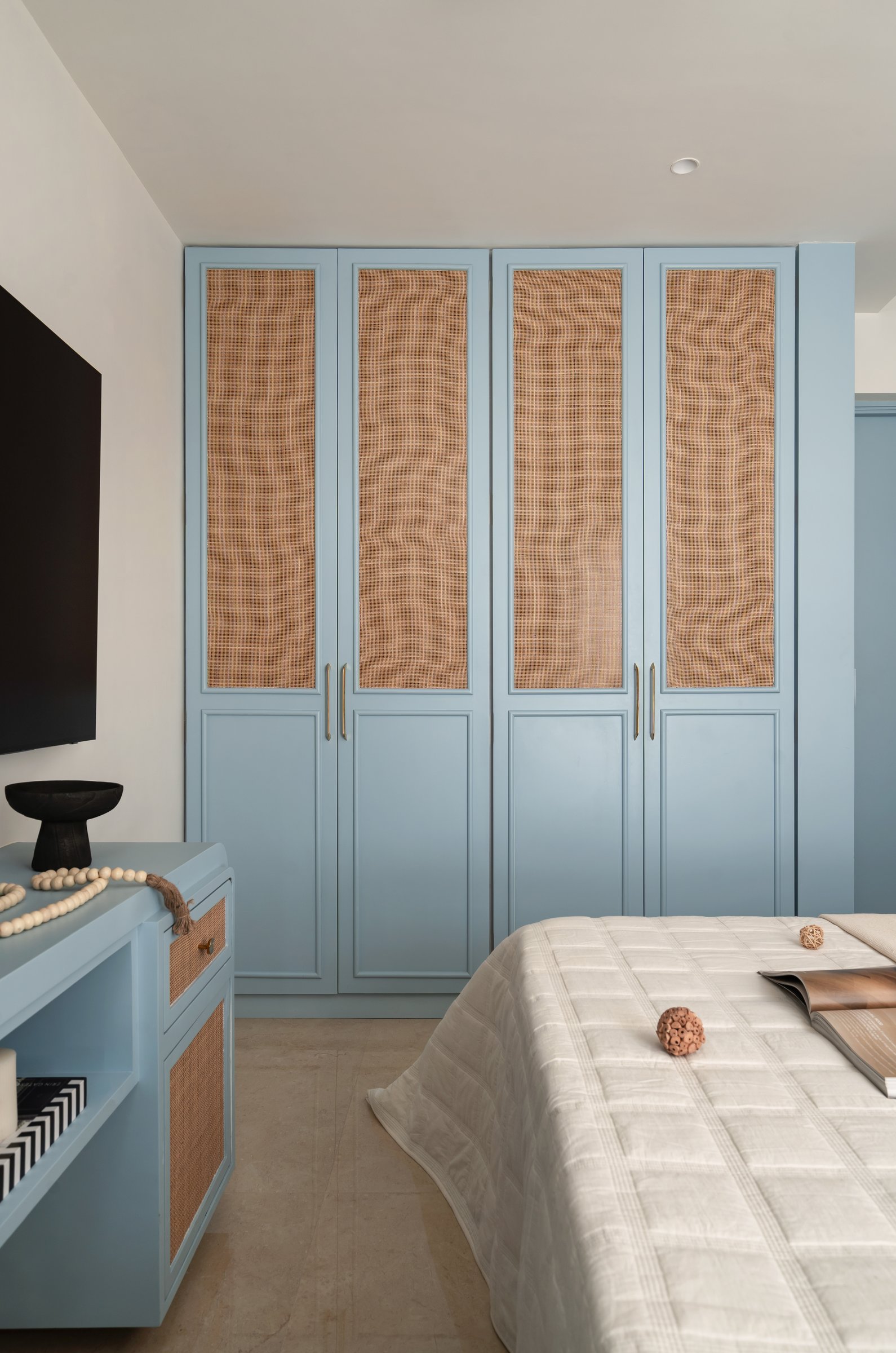 A full-height wardrobe in dusty blue with woven cane inset panels and brass pulls