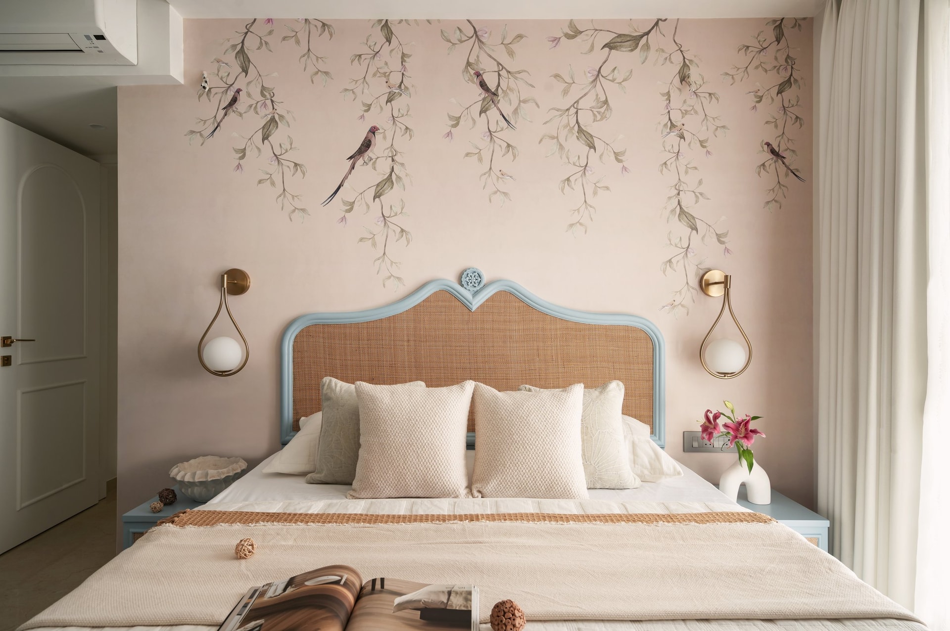 The primary bedroom, where a cane headboard framed in dusty blue sits beneath a botanical wallpaper