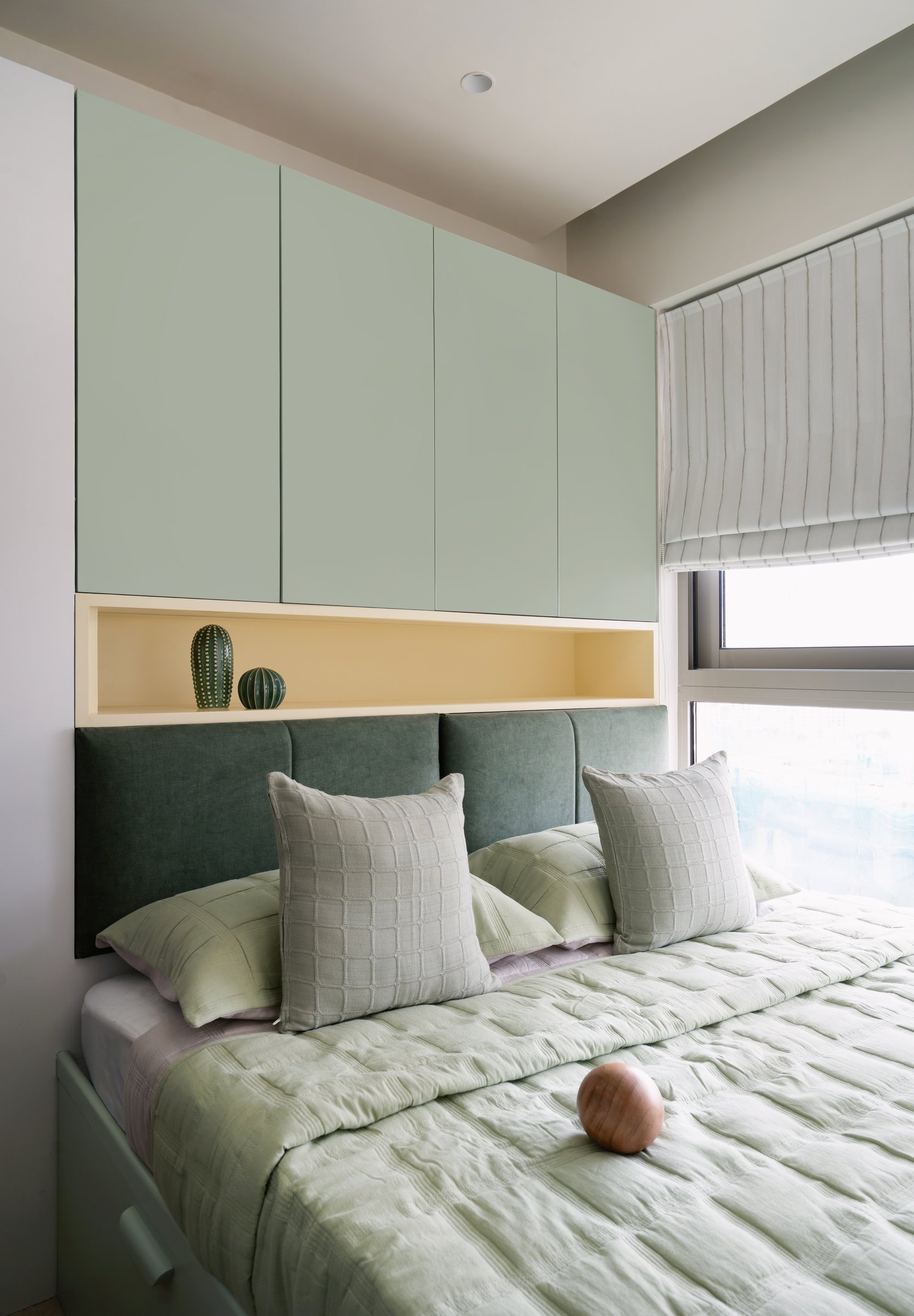 In the second bedroom, sage cabinetry floats above a warm yellow niche and a deep green upholstered headboard