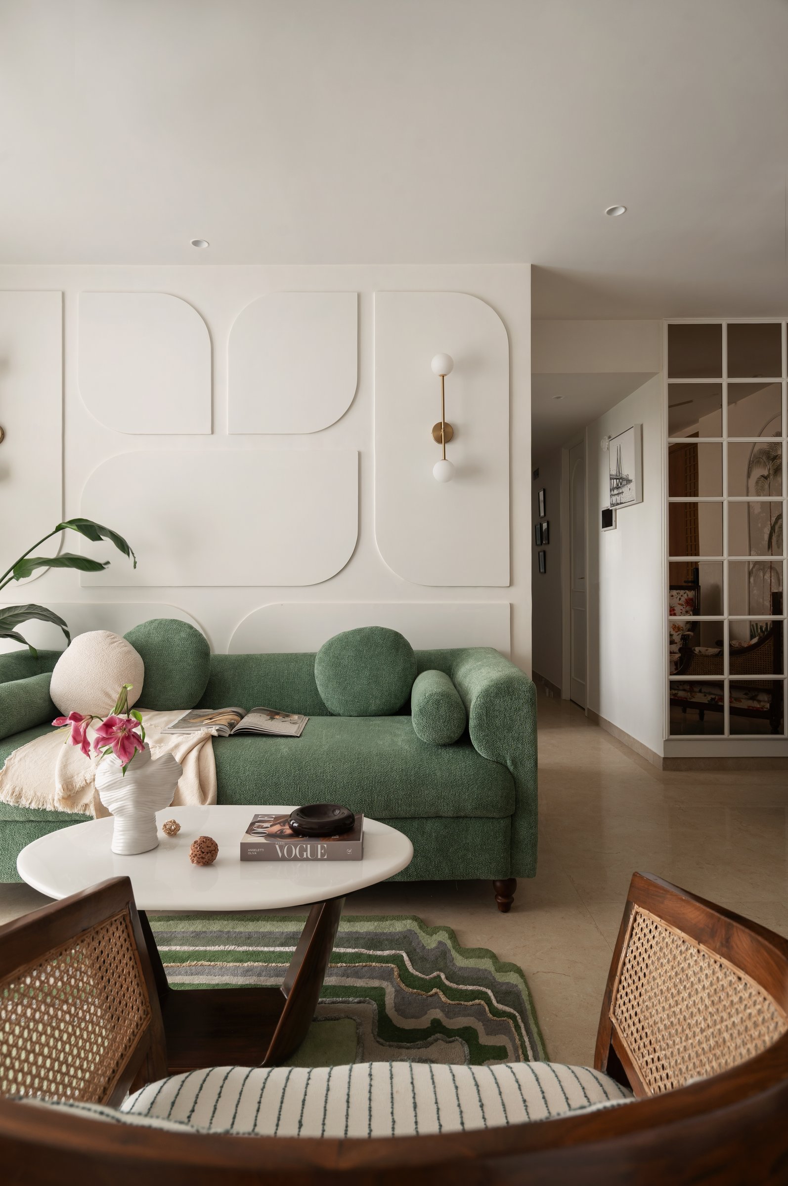 The living room, where a deep green bouclé sofa meets a sculptural wall of interlocking curved relief panels