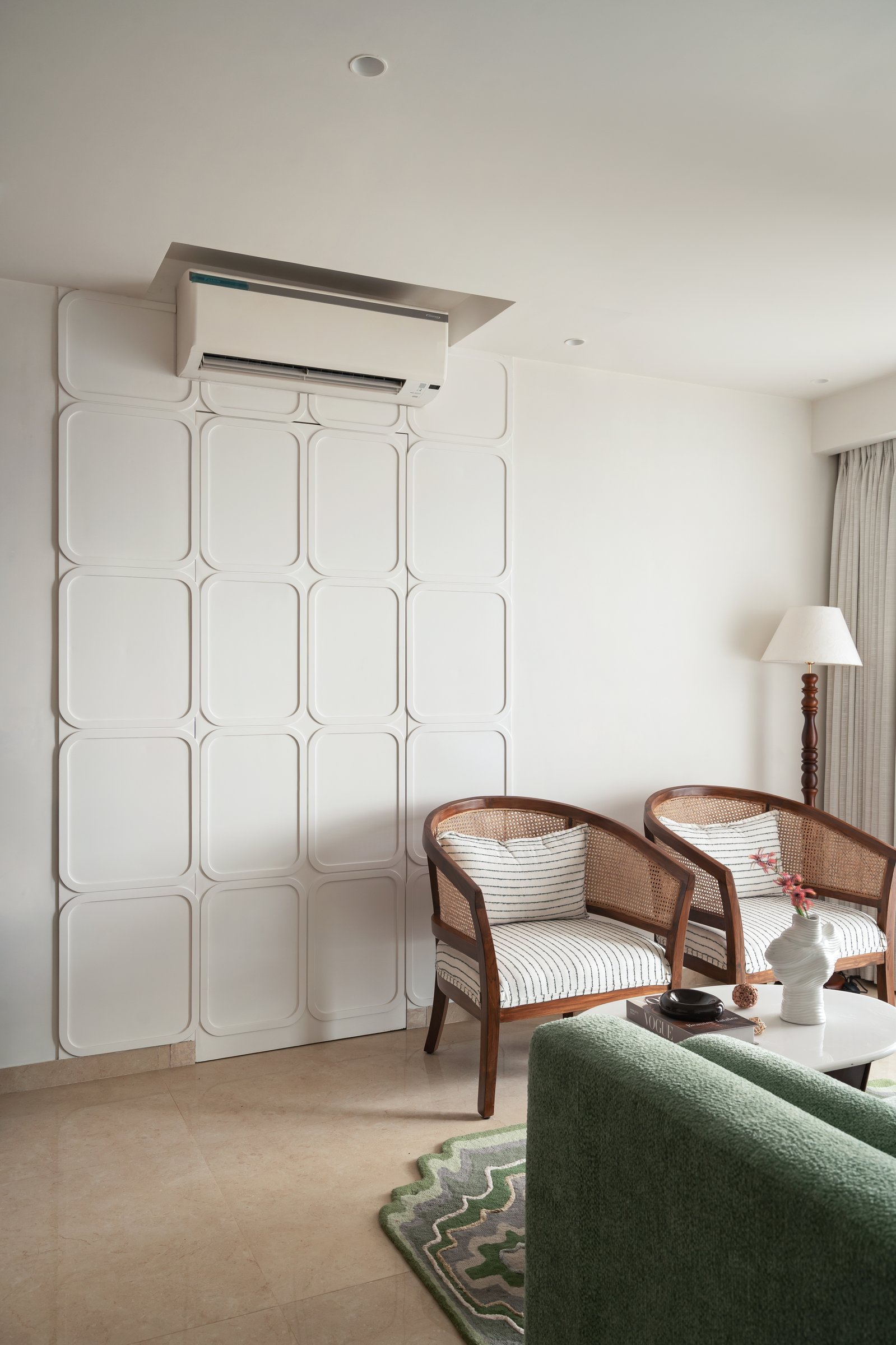 Cane-backed wooden armchairs anchor the second seating group against a panelled surface that absorbs the AC unit