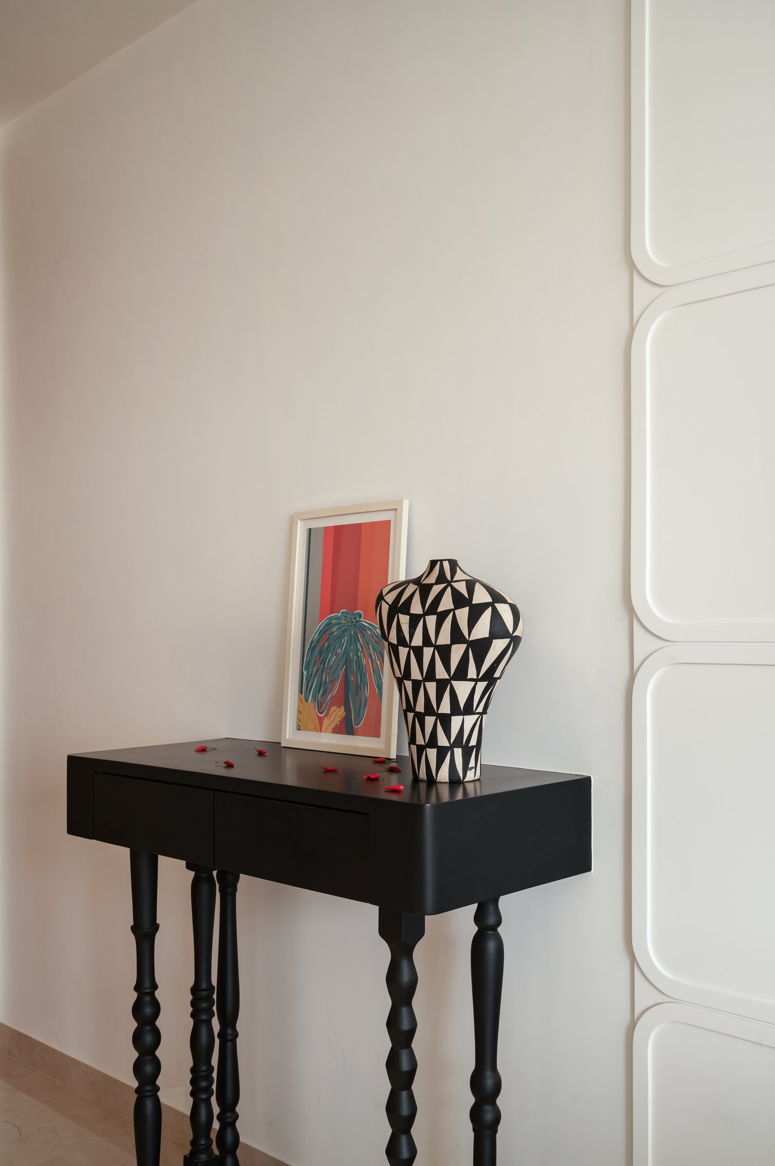 A slender black console with turned legs holds a monochrome vessel against the home's recurring curved panelling