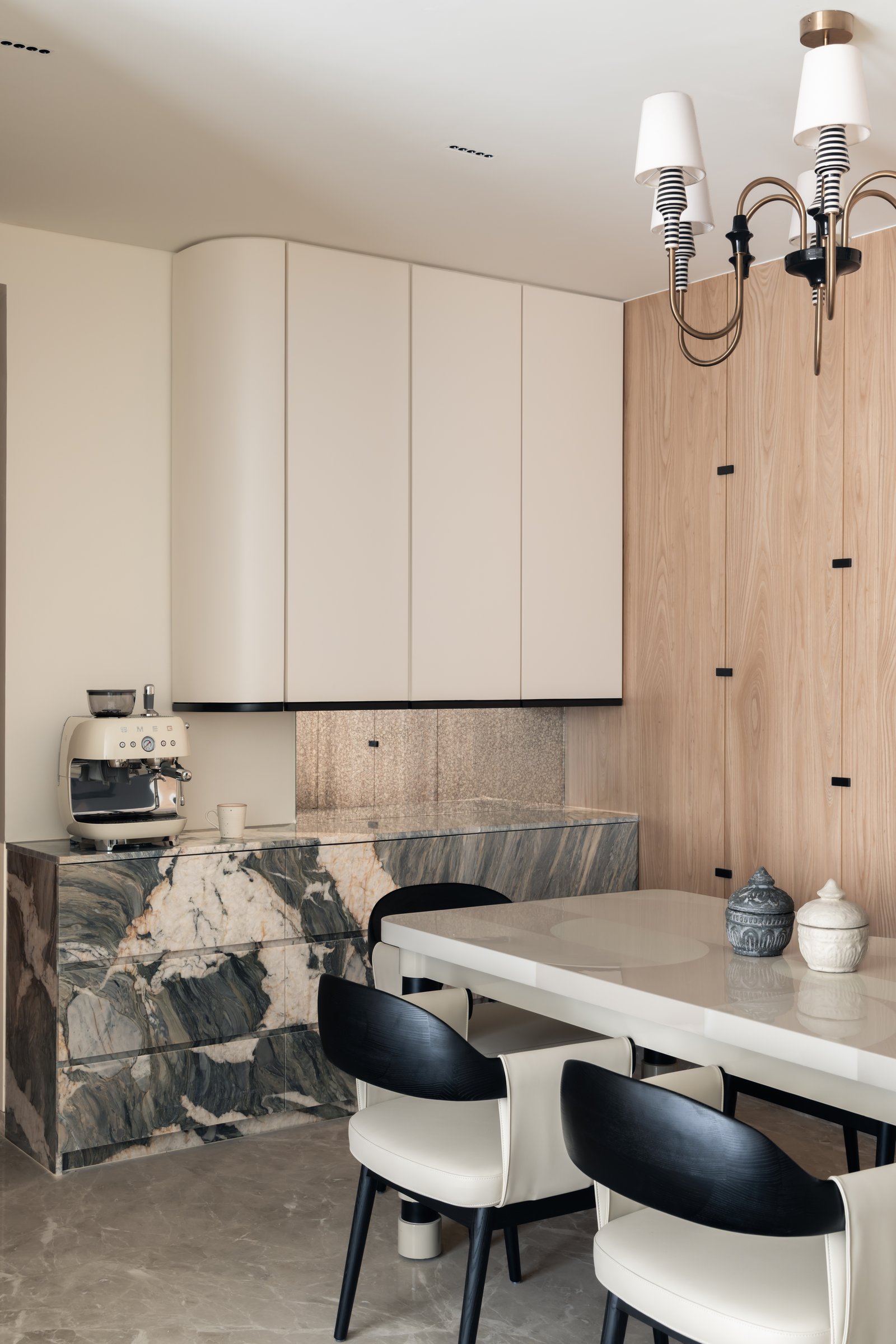 The kitchen island, clad in dramatically veined stone with a mother-of-pearl backsplash and softly curved cabinetry above