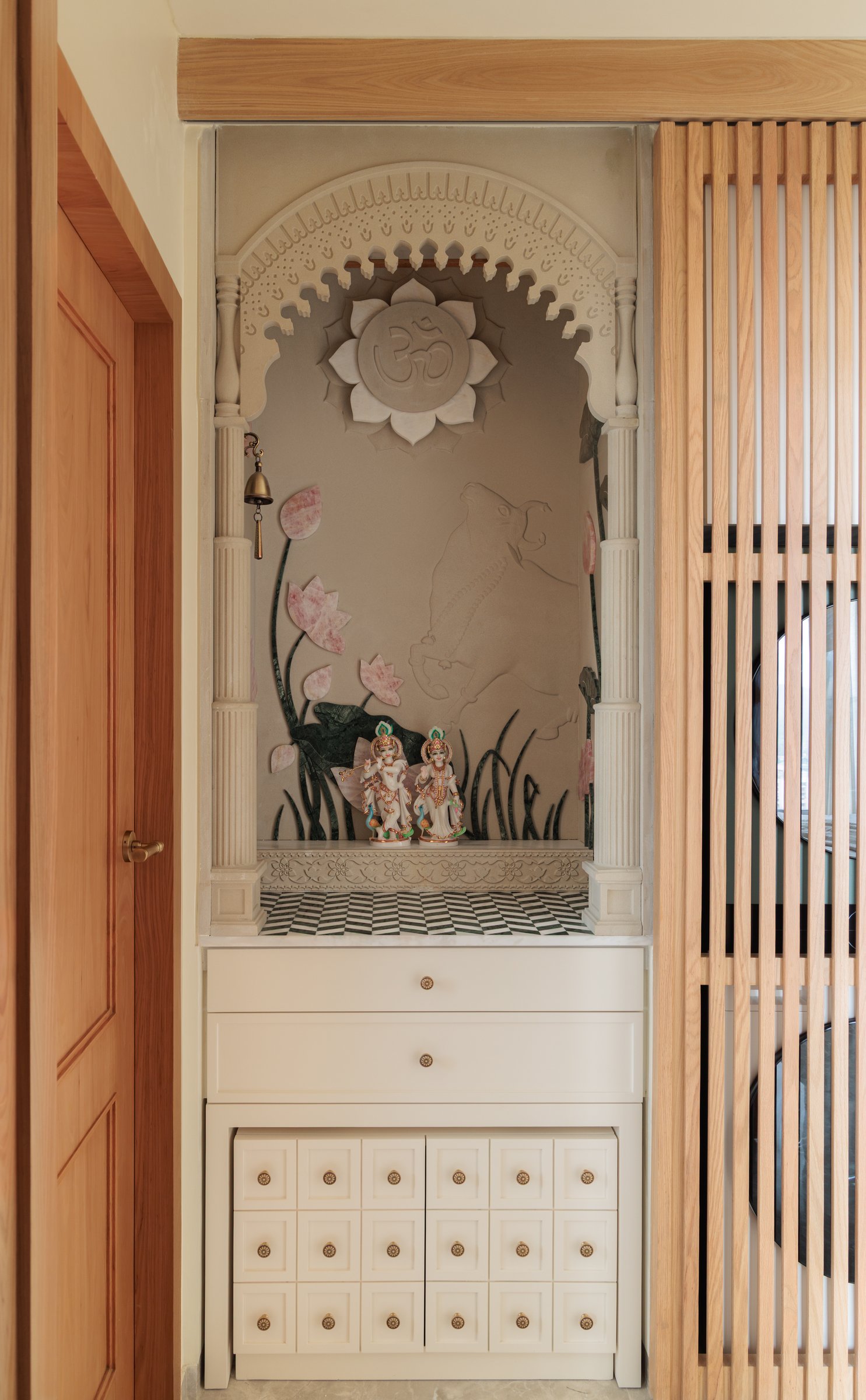 The puja alcove, set behind a slatted wooden screen within a hand-sculpted plaster arch