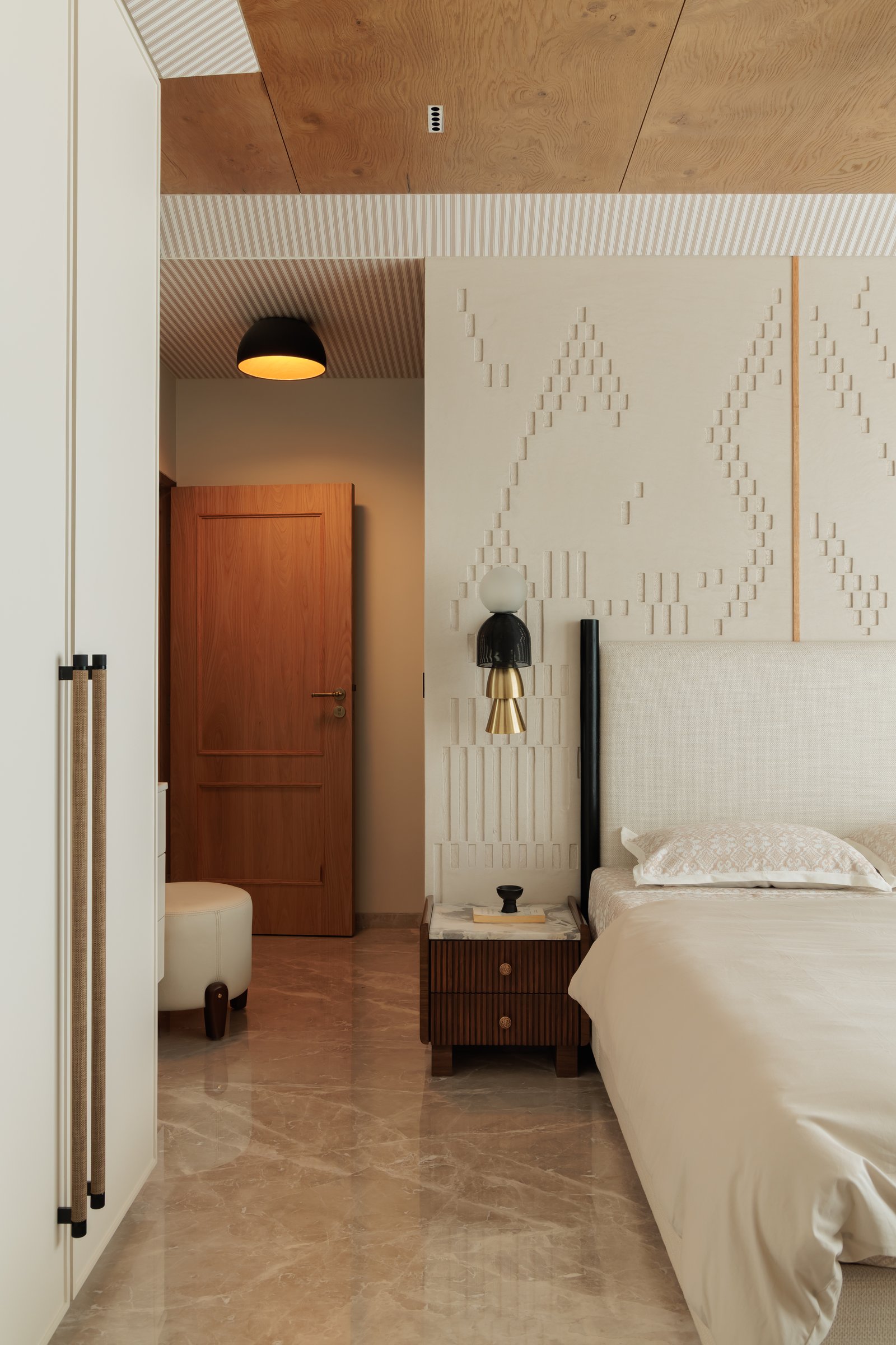 The master bedroom, where a hand-worked textured plaster wall carries a diagonal woven motif framed in slim wooden battens